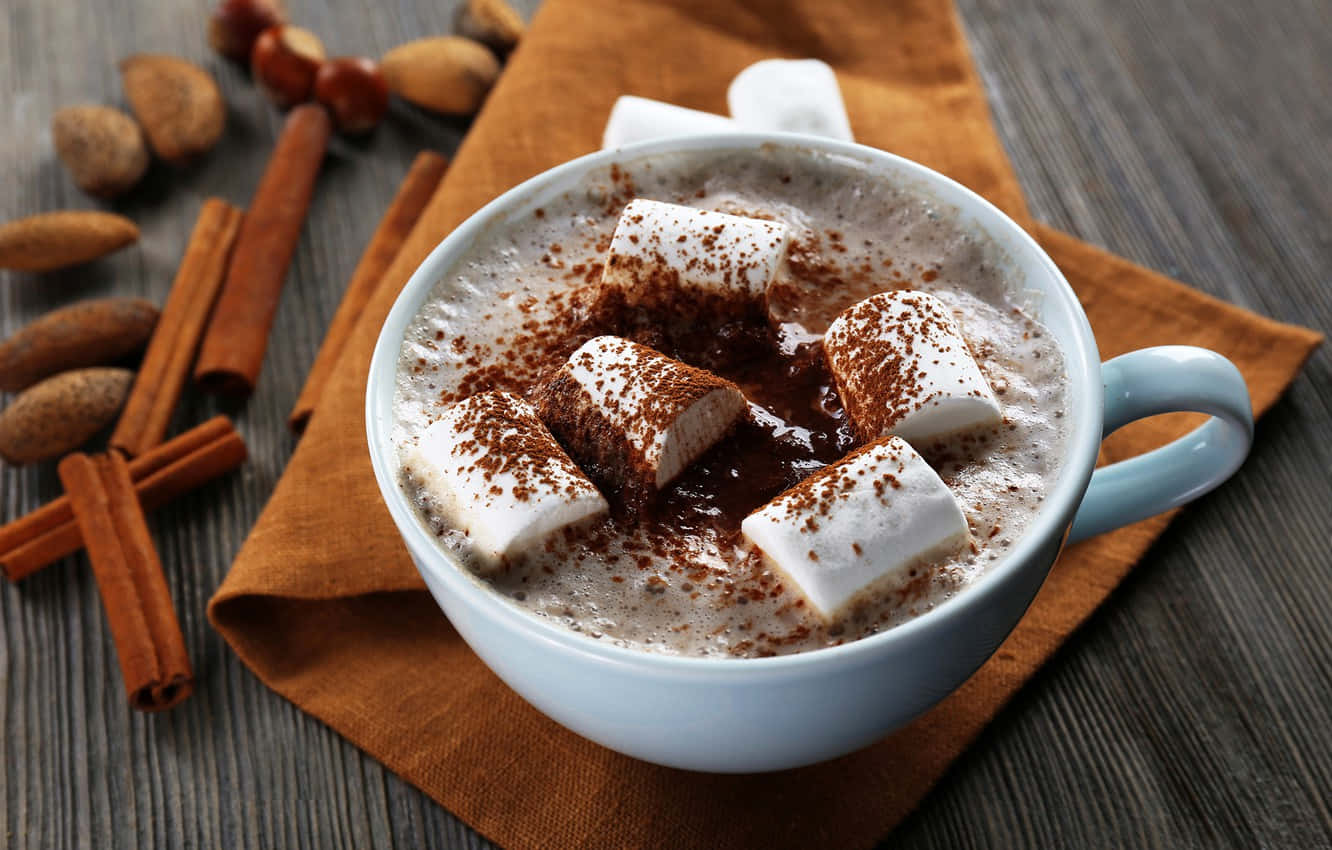 Milk And Coffee 桌布 壁紙 — 一杯冒著熱氣的熱朱古力，上面放著棉花糖和肉桂，放在一張散落著堅果和香料的木桌上。