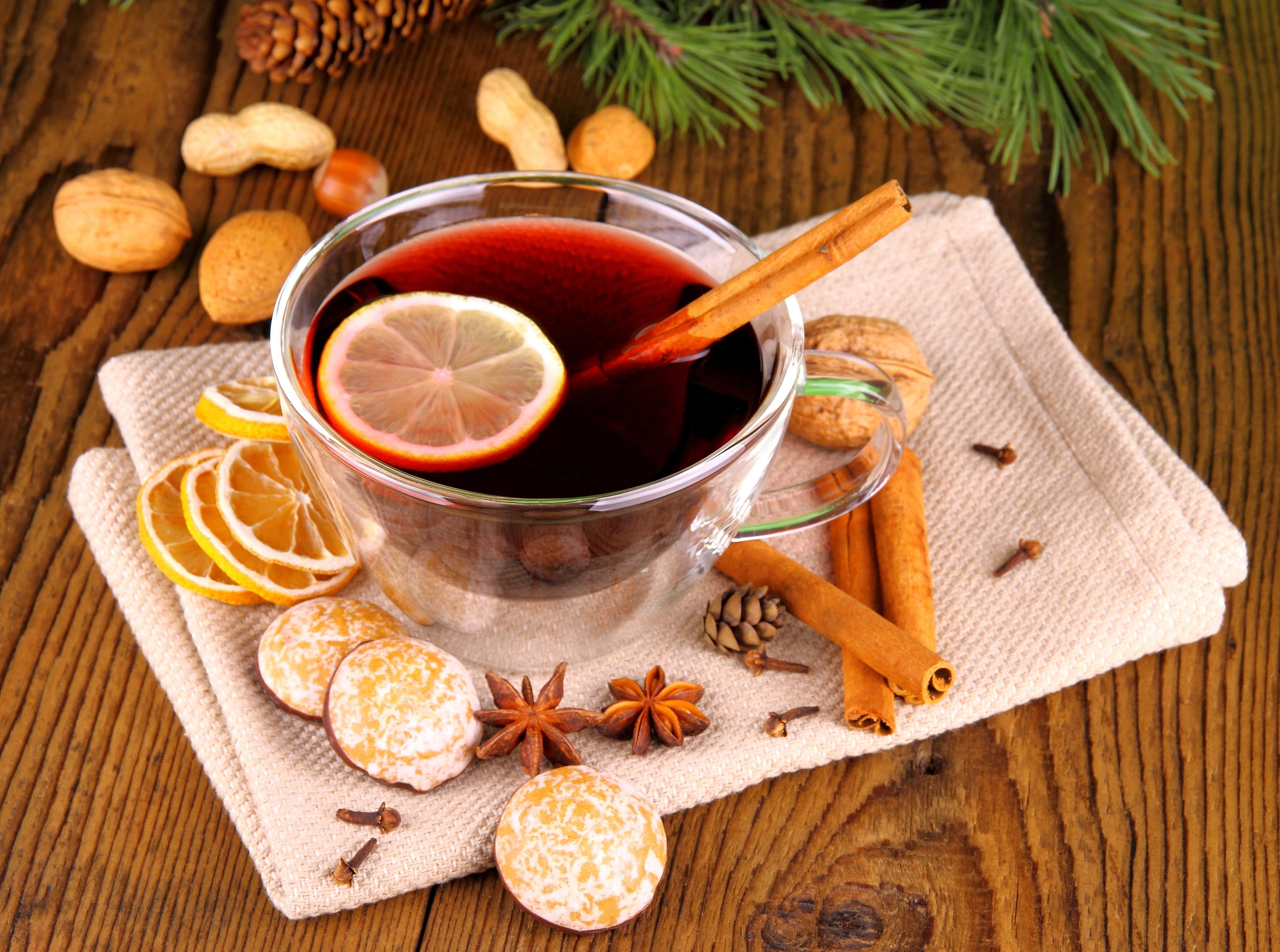 Mulled Wine 桌布 壁紙 — 一杯冒著熱氣的香料熱紅酒，飾以檸檬和肉桂，放在木桌上，周圍環繞著節日冬季香料和松針。