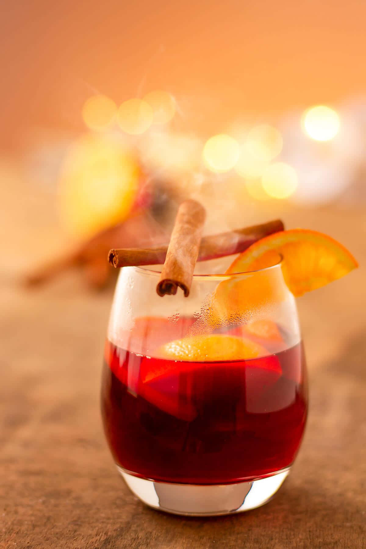 Winter Drinks 桌布 壁紙 — 一杯冒著熱氣的香料熱紅酒，飾以肉桂棒和橙片，在散景燈光背景下溫暖地發光。