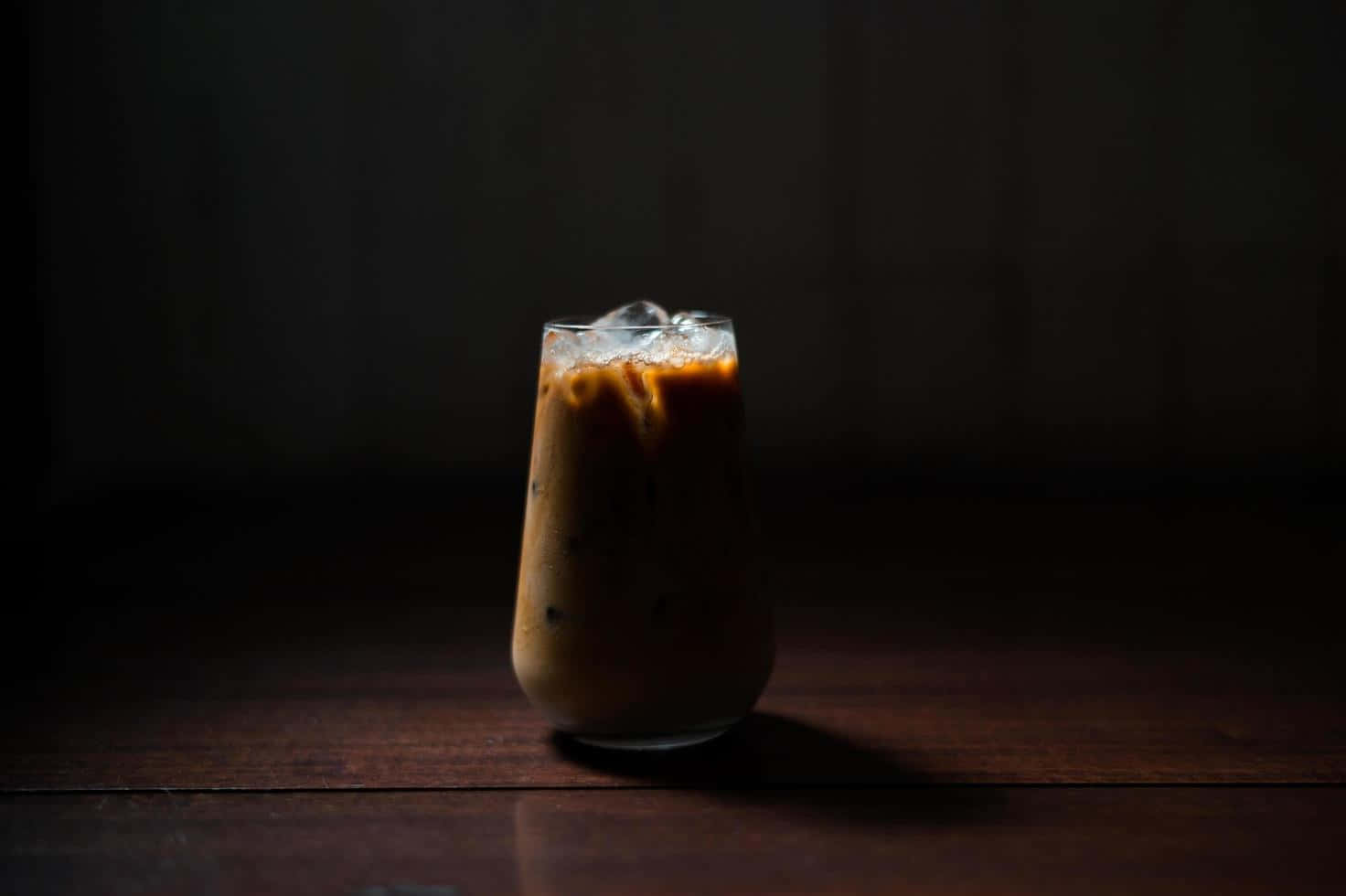 Milk And Coffee 桌布 壁紙 — 一杯加冰的凍咖啡放在深色木桌上，在戲劇性的低調燈光下。