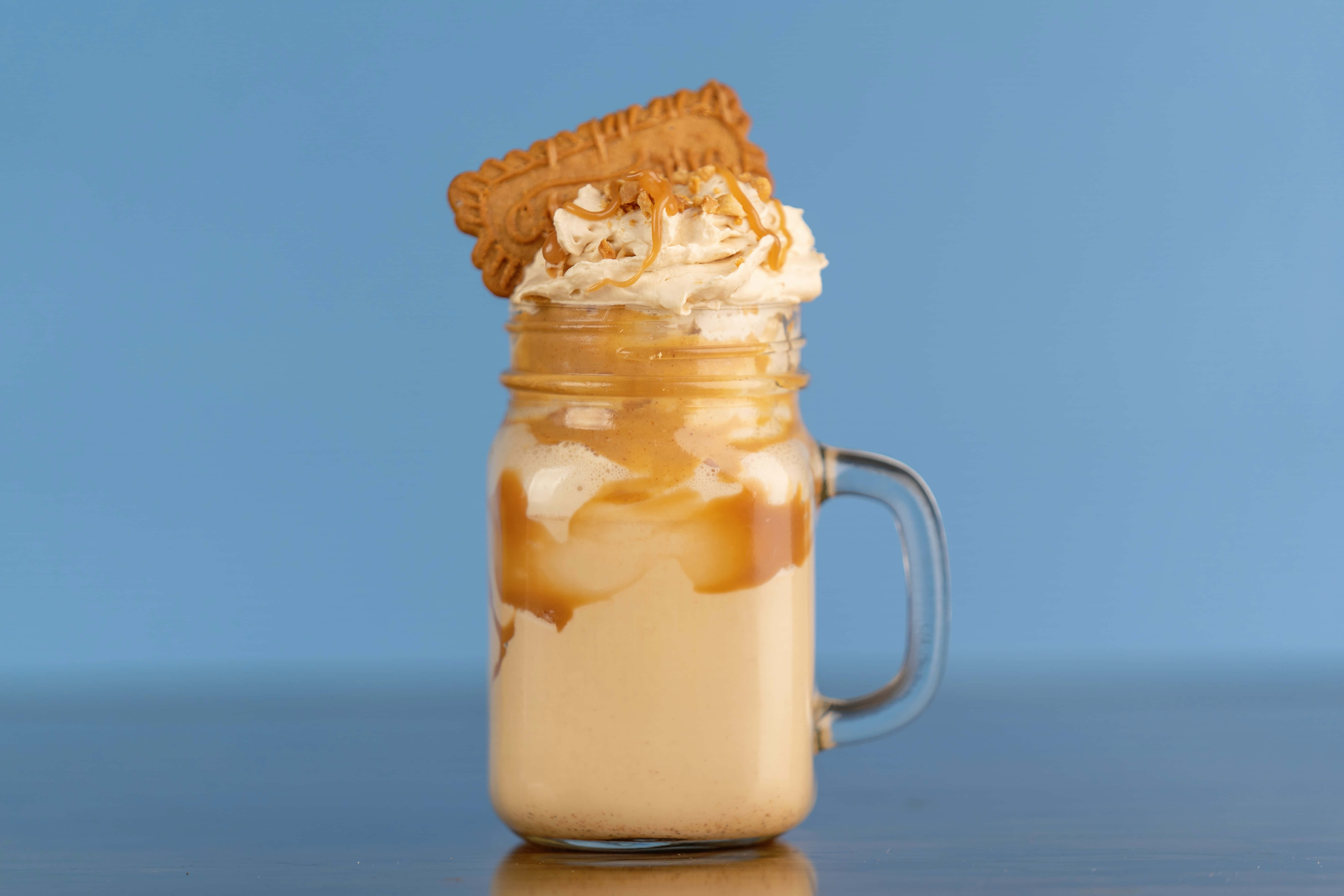 Caramel 桌布 壁紙 — 一杯奶油焦糖冰咖啡放在梅森罐中，上面加上忌廉、焦糖醬和餅乾，背景為純藍色。
