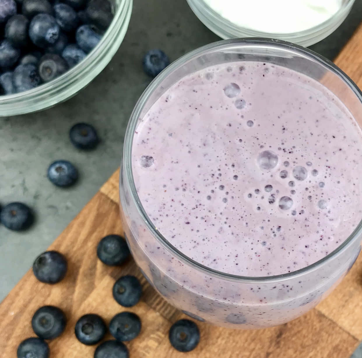 Blueberry Smoothie 桌布 壁紙 — 一杯泡沫紫色藍莓奶昔放在木板上，周圍是新鮮藍莓和乳酪。