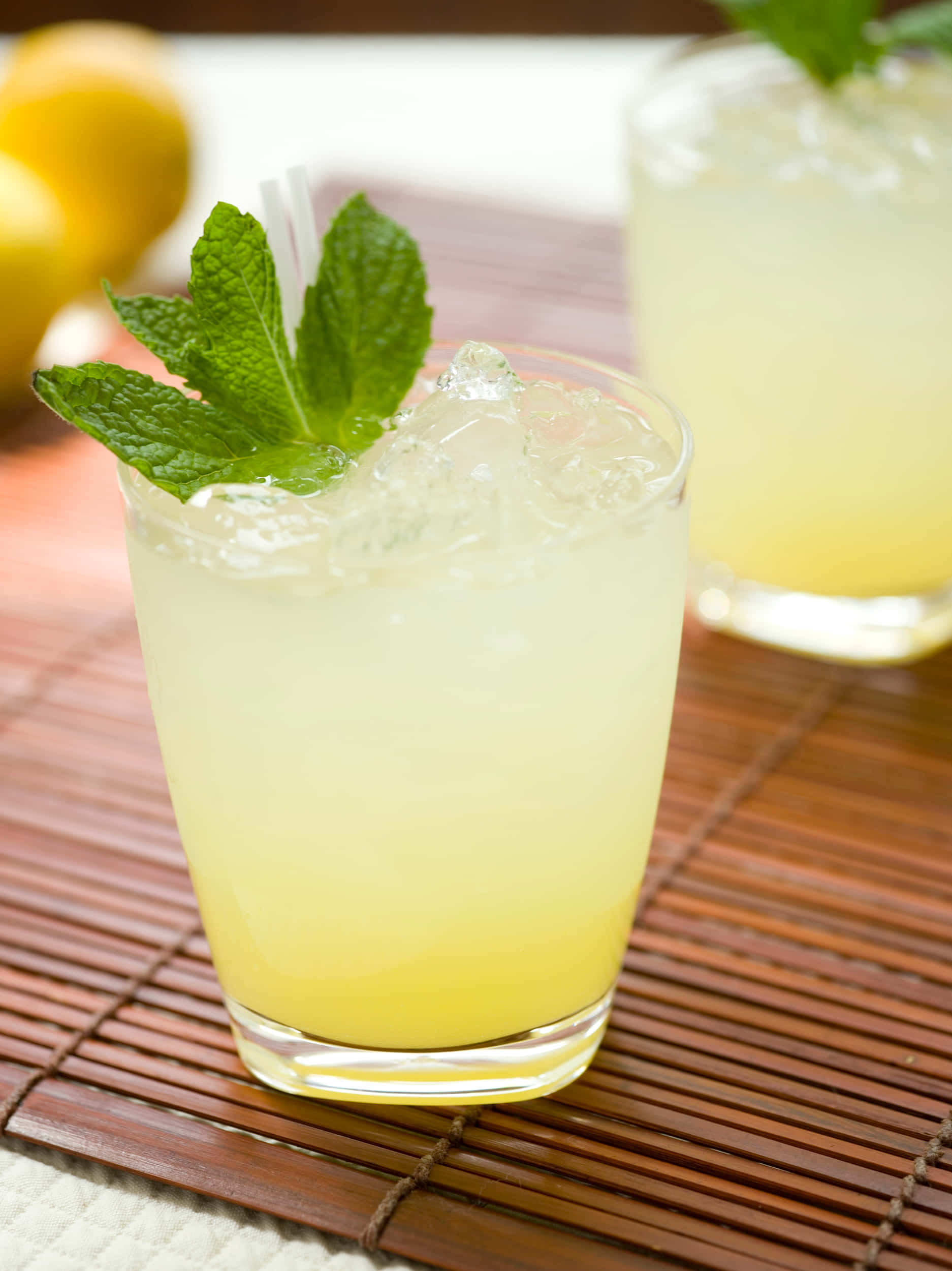 Winter Drinks 桌布 壁紙 — 一杯清爽的檸檬水，加入薄荷和冰塊，放在竹蓆上，背景有檸檬，柔焦效果。