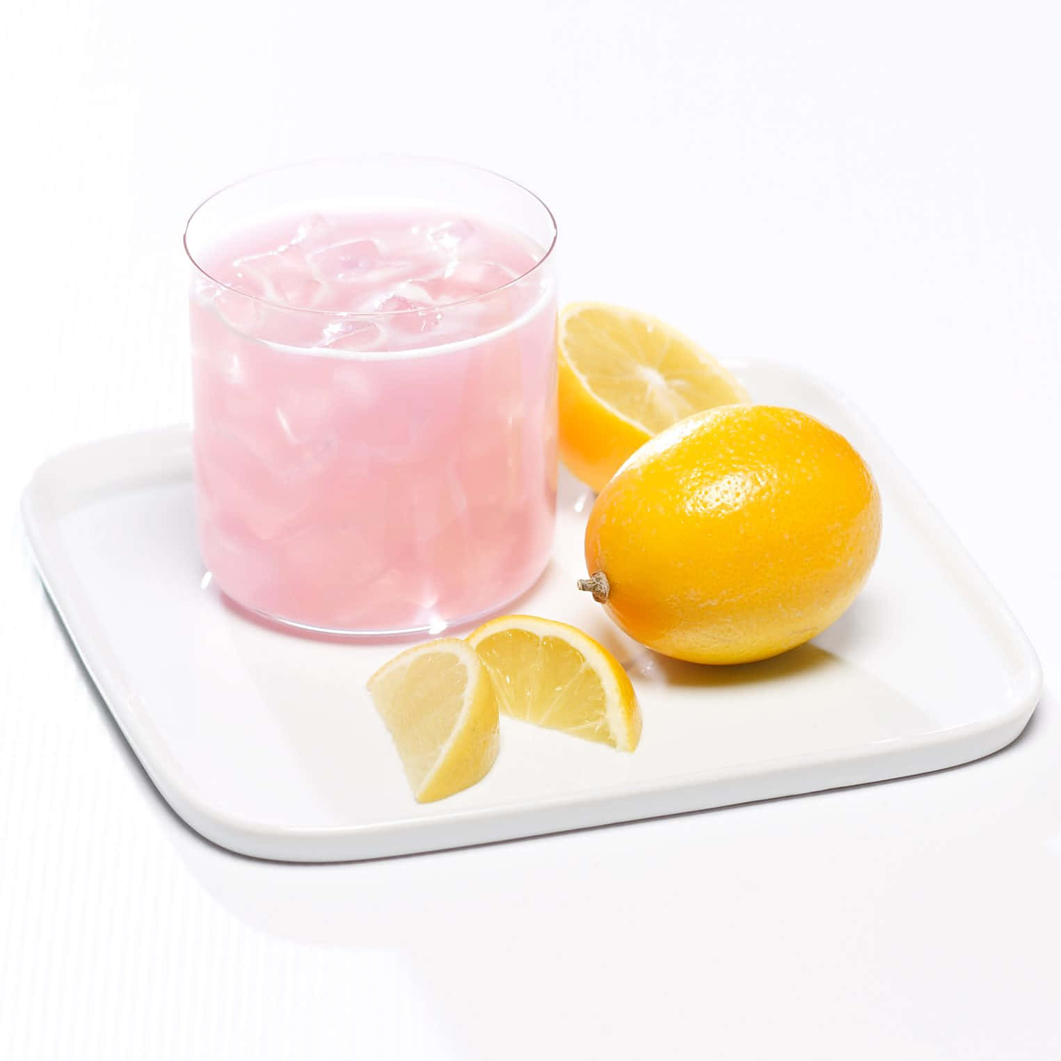 Pink Lemonade 桌布 壁紙 — 一杯清爽的粉紅檸檬水加冰放在白色托盤上，旁邊有完整和切片的檸檬，背景是潔淨的白色。