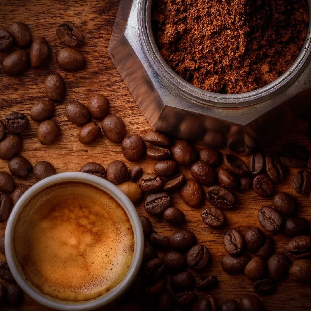 Brown Coffee 桌布 壁紙 — 一杯濃郁的意式濃縮咖啡放在一個六角形研磨機旁邊，研磨機裡裝滿了深色咖啡渣和散落的咖啡豆，置於質樸的木質表面上。