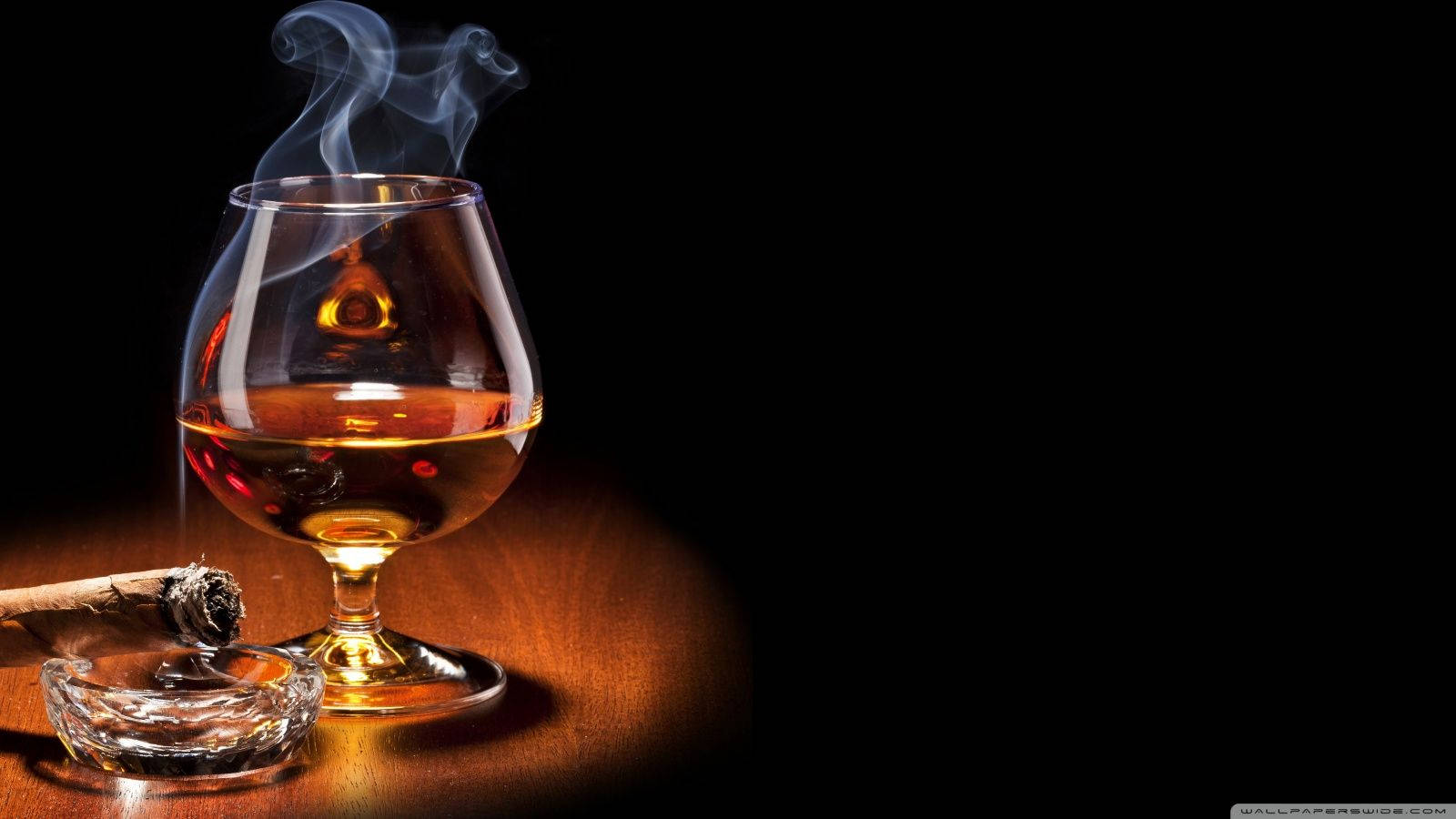 飲品 桌布 壁紙 — 一杯煙霧繚繞的琥珀色威士忌在黑色背景的木桌上，旁邊的水晶煙灰缸裡放著一支點燃的雪茄，散發著溫暖的光芒。