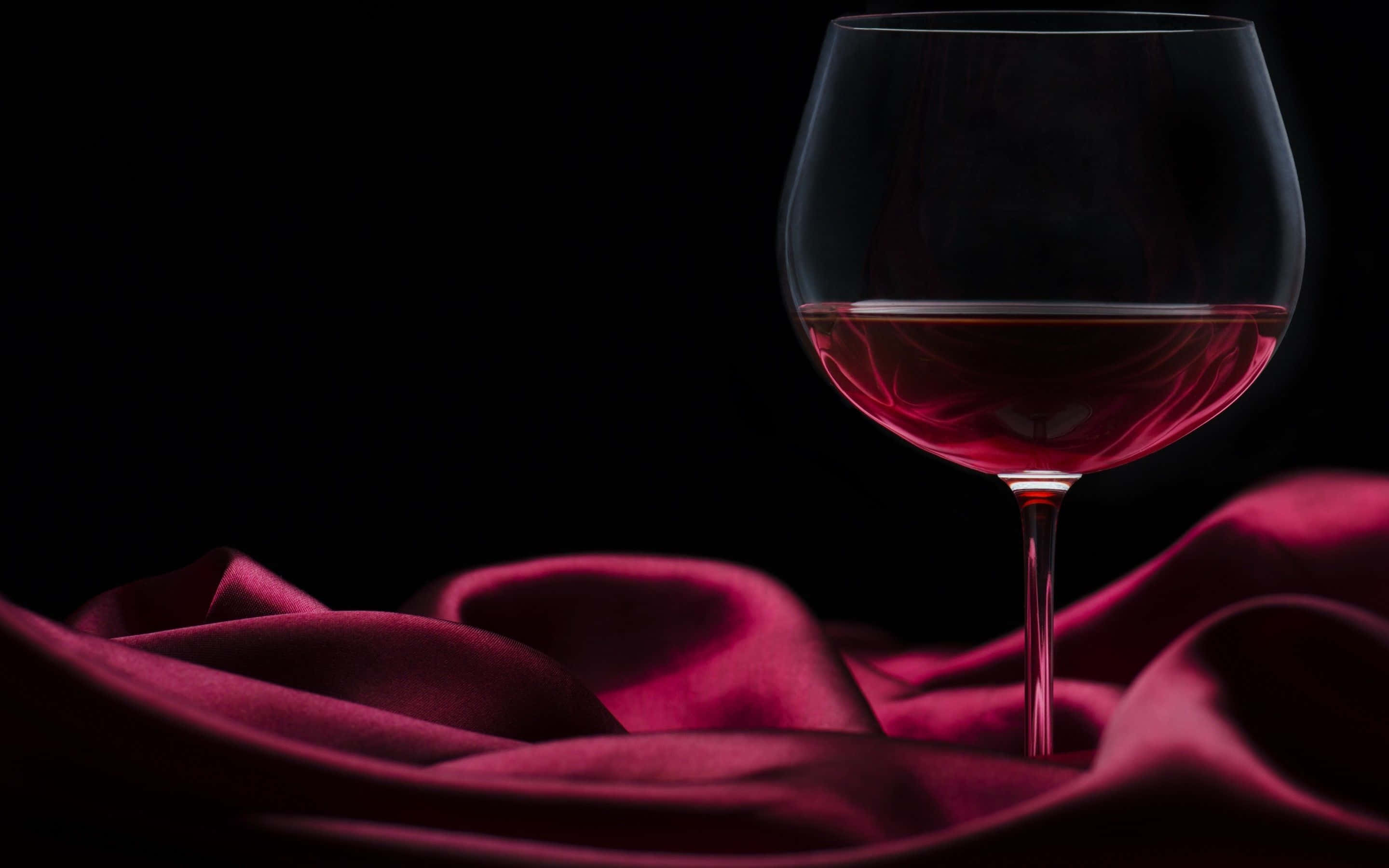 Red Wine Glass 桌布 壁紙 — 一杯紅酒優雅地放在豐富的酒紅色緞面布料上，背景是純黑色。