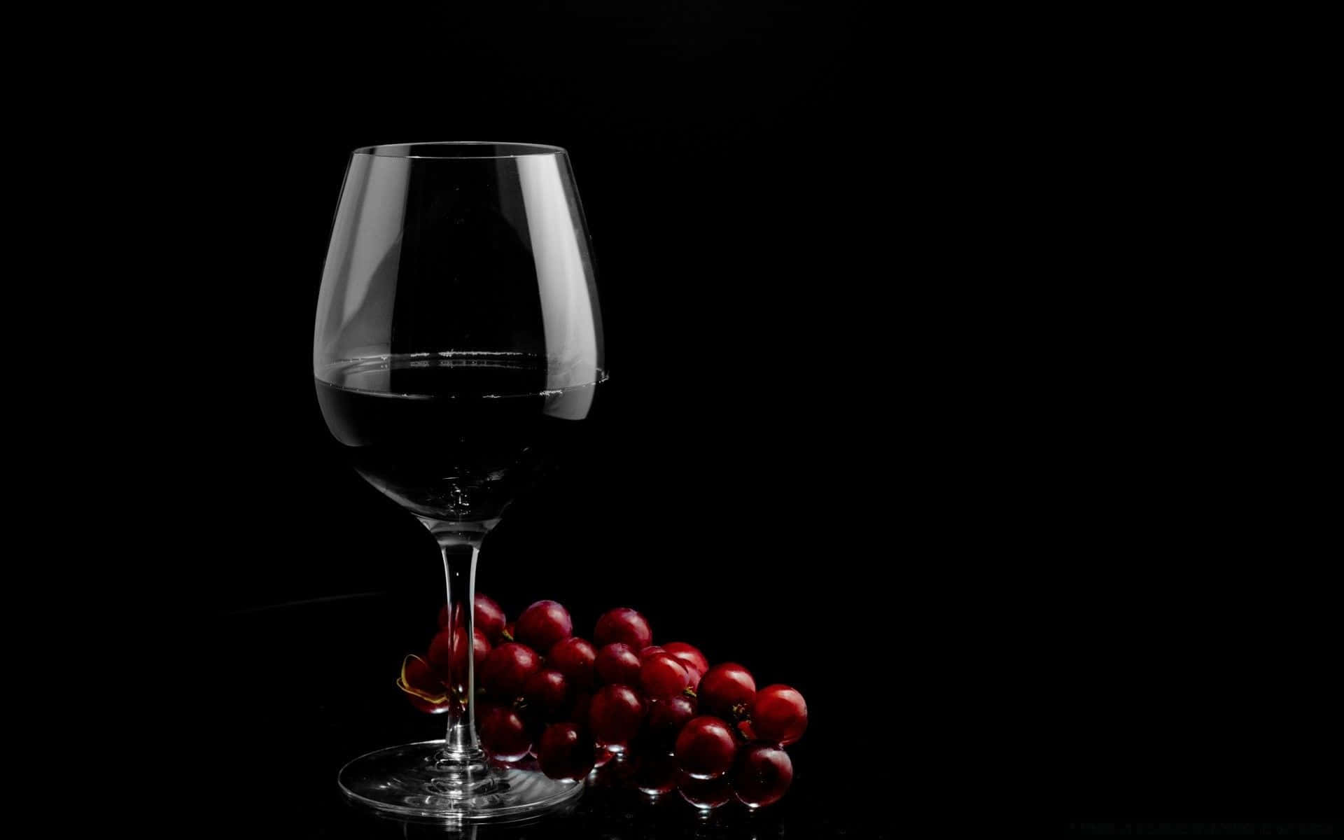 Black Wine 桌布 壁紙 — 一杯紅酒和一串紅葡萄在柔和光線下，在純黑背景中閃耀。