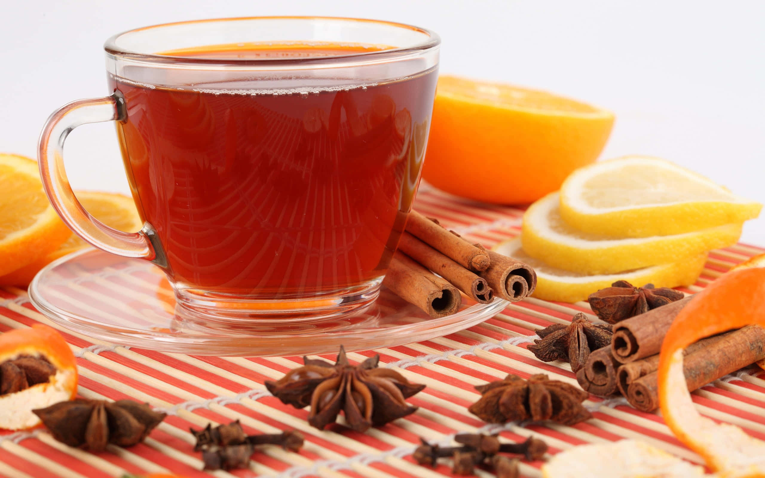 Mulled Wine 桌布 壁紙 — 一杯透明玻璃杯裝著的香料茶放在條紋墊上，周圍有柑橘片、肉桂棒和八角。