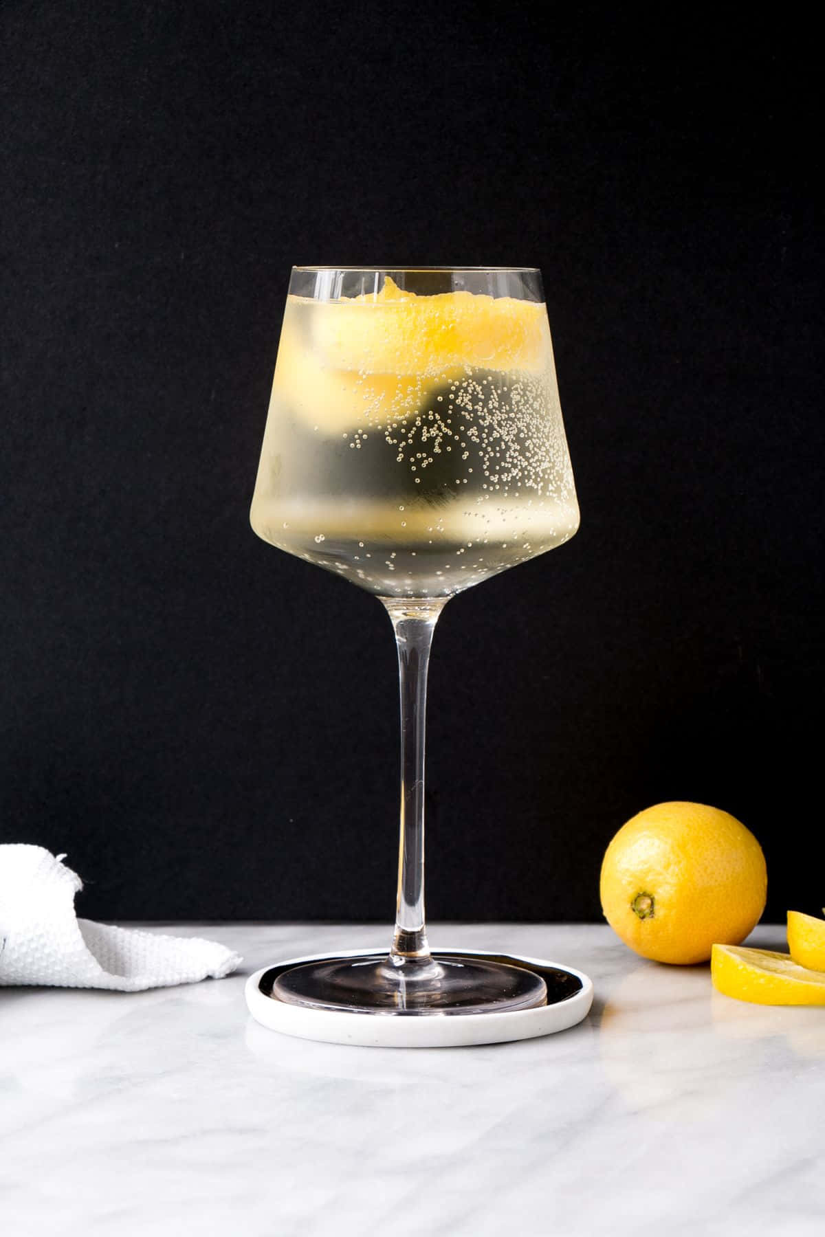 White Wine 桌布 壁紙 — 一杯閃閃發光的檸檬雞尾酒放在酒杯中，置於大理石表面上，旁邊是新鮮檸檬，背景為黑色。