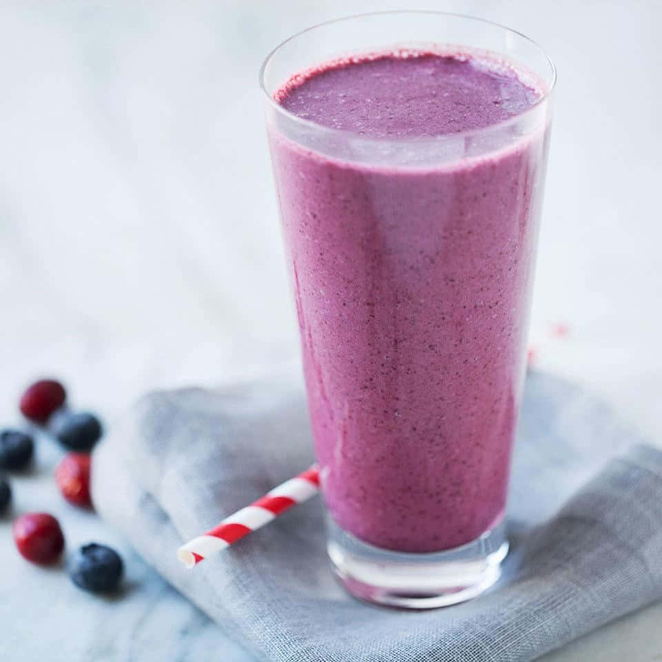 Blueberry Smoothie 桌布 壁紙 — 一杯高身嘅紫色莓果冰沙，插住紅白間條飲管，放喺灰色布上面，旁邊散落住藍莓同紅莓。