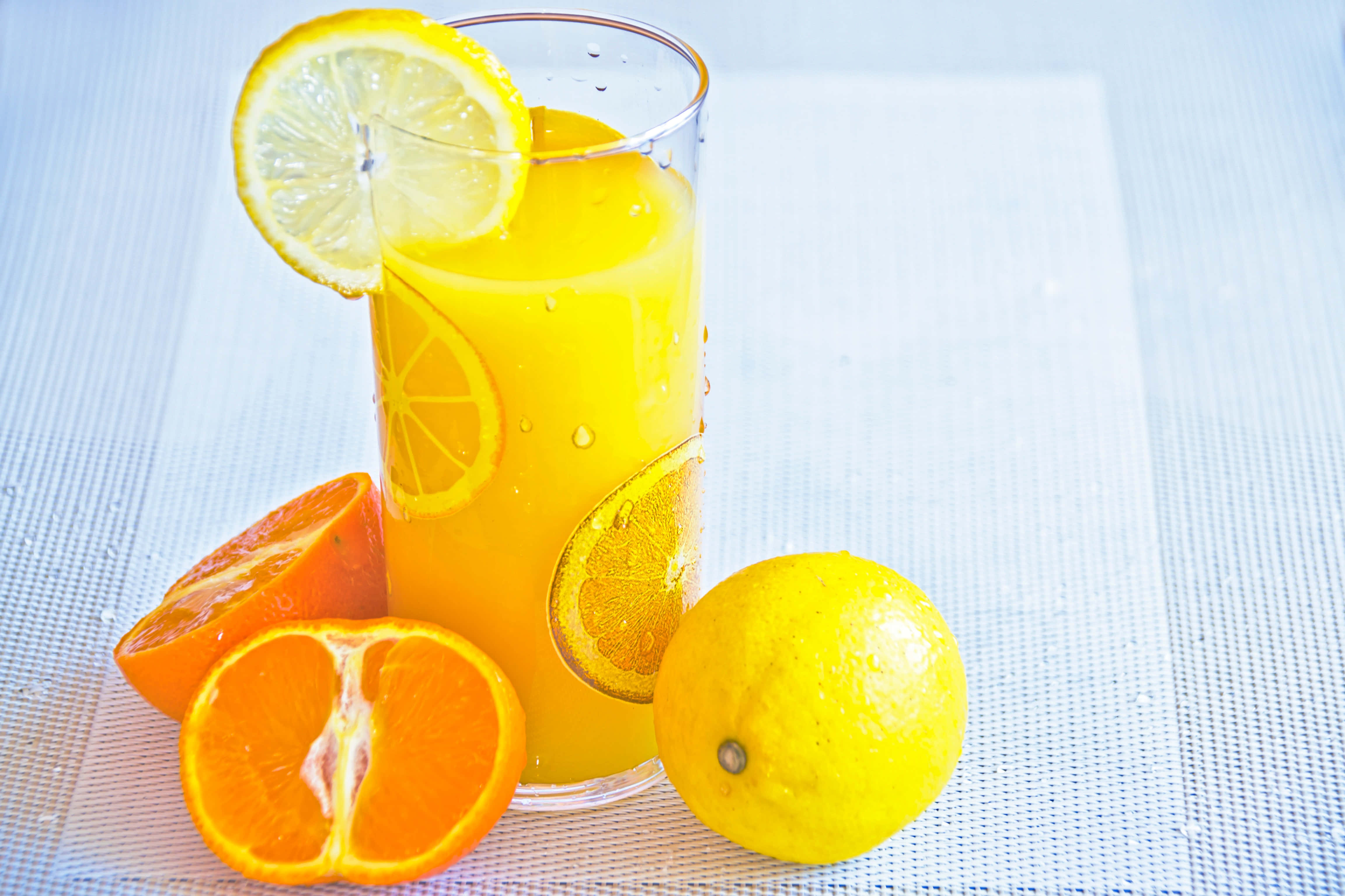 Summer Drinks 桌布 壁紙 — 一杯高身鮮橙汁，飾以檸檬和橙片，旁邊放上新鮮柑橘類水果，置於有紋理的白色表面上。