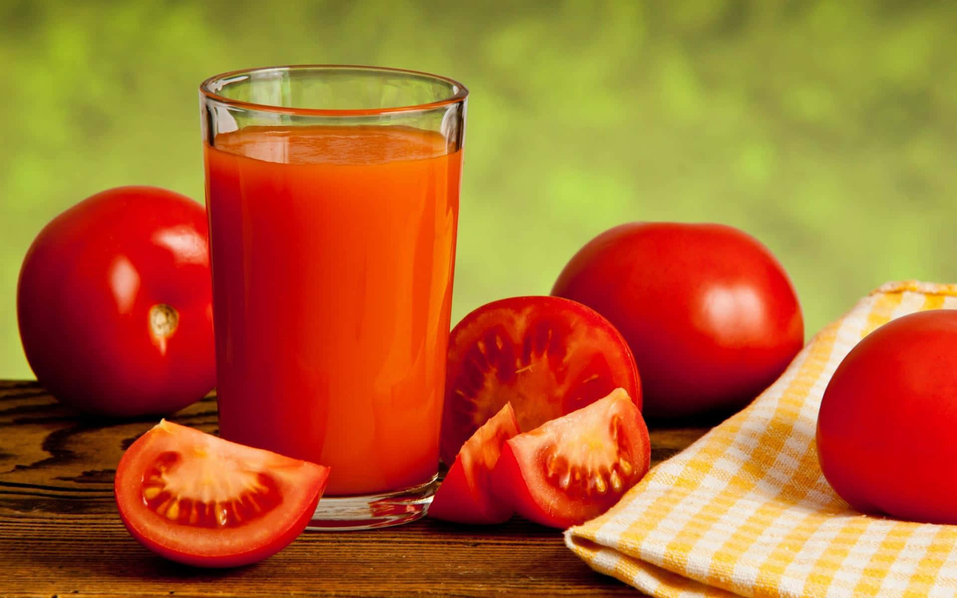 tomato 桌布 壁紙 — 一杯鮮紅色的番茄汁放在木桌上，旁邊有新鮮的完整番茄和切片番茄，桌上鋪著黃色格紋桌布。