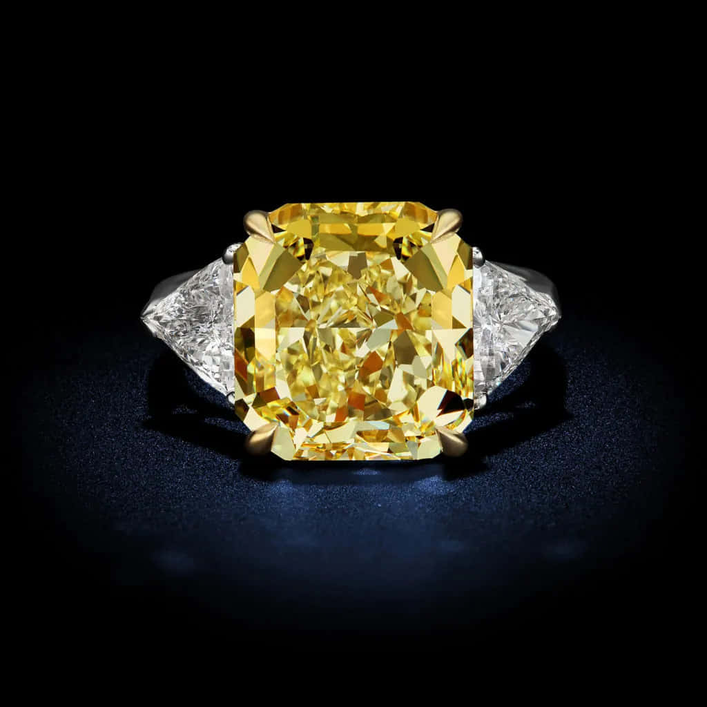 Yellow Diamond 桌布 壁紙 — 一枚令人驚嘆的枕形切割黃鑽戒指，搭配兩顆透明鑽石，置於深藍色天鵝絨表面上。