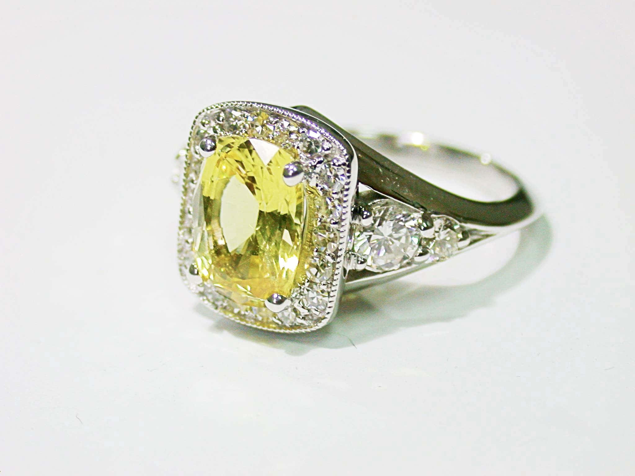 Yellow Sapphire 桌布 壁紙 — 一枚令人驚嘆的黃色寶石戒指，帶有鑽石光環和側面裝飾，在純淨的白色背景上閃耀。