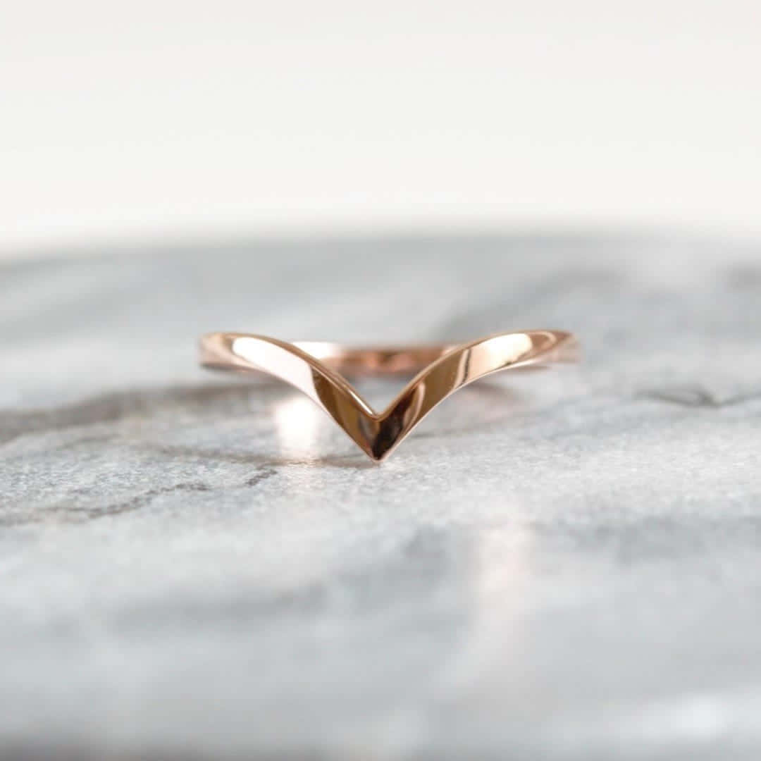 Wedding Rings 桌布 壁紙 — 一枚時尚的玫瑰金V形戒指，置於清涼的灰色大理石表面上，配以柔和燈光。