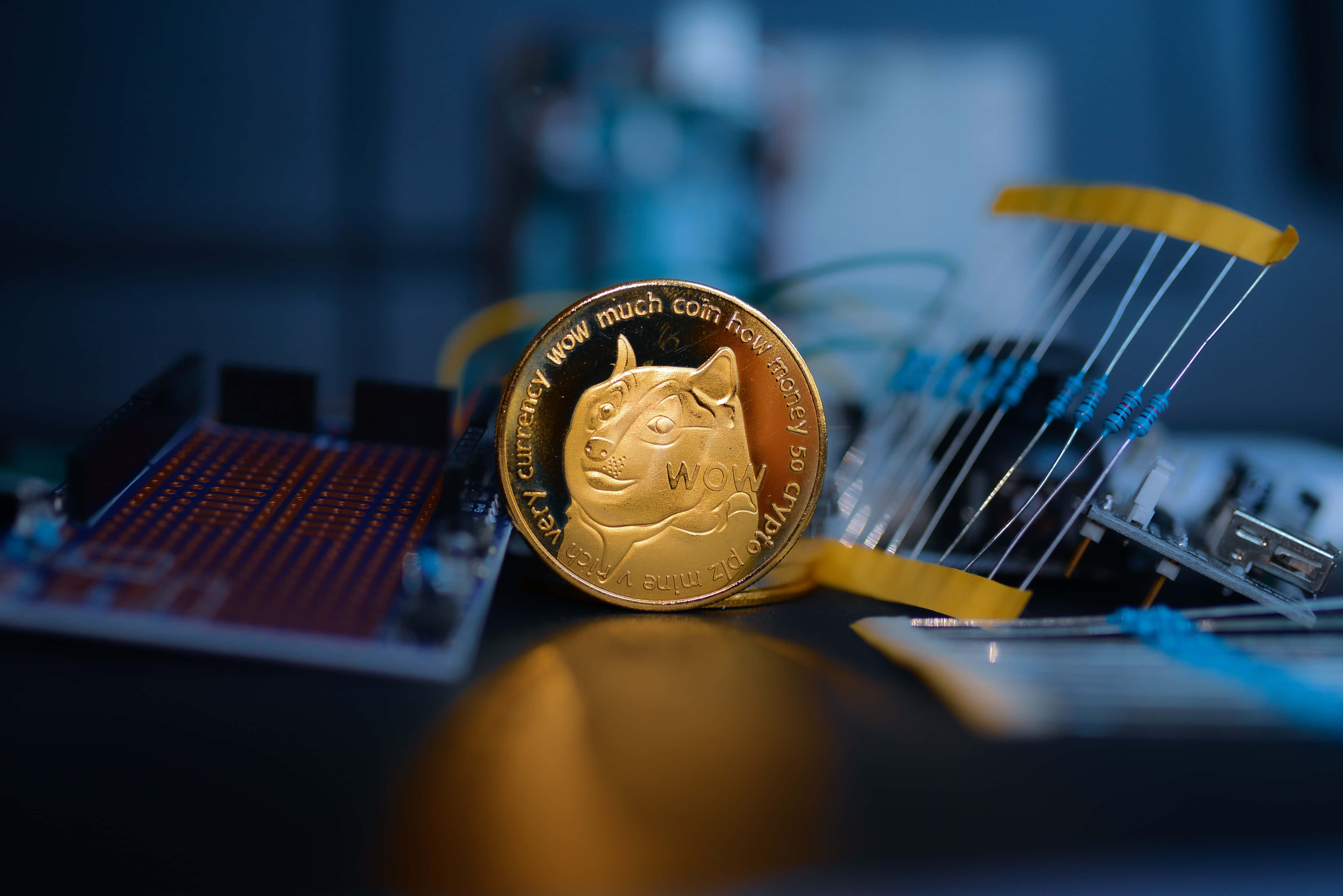 Dogecoin 桌布 壁紙 — 一枚金色 Dogecoin 放在電路板上，周圍是電子元件，在冷藍燈光下。