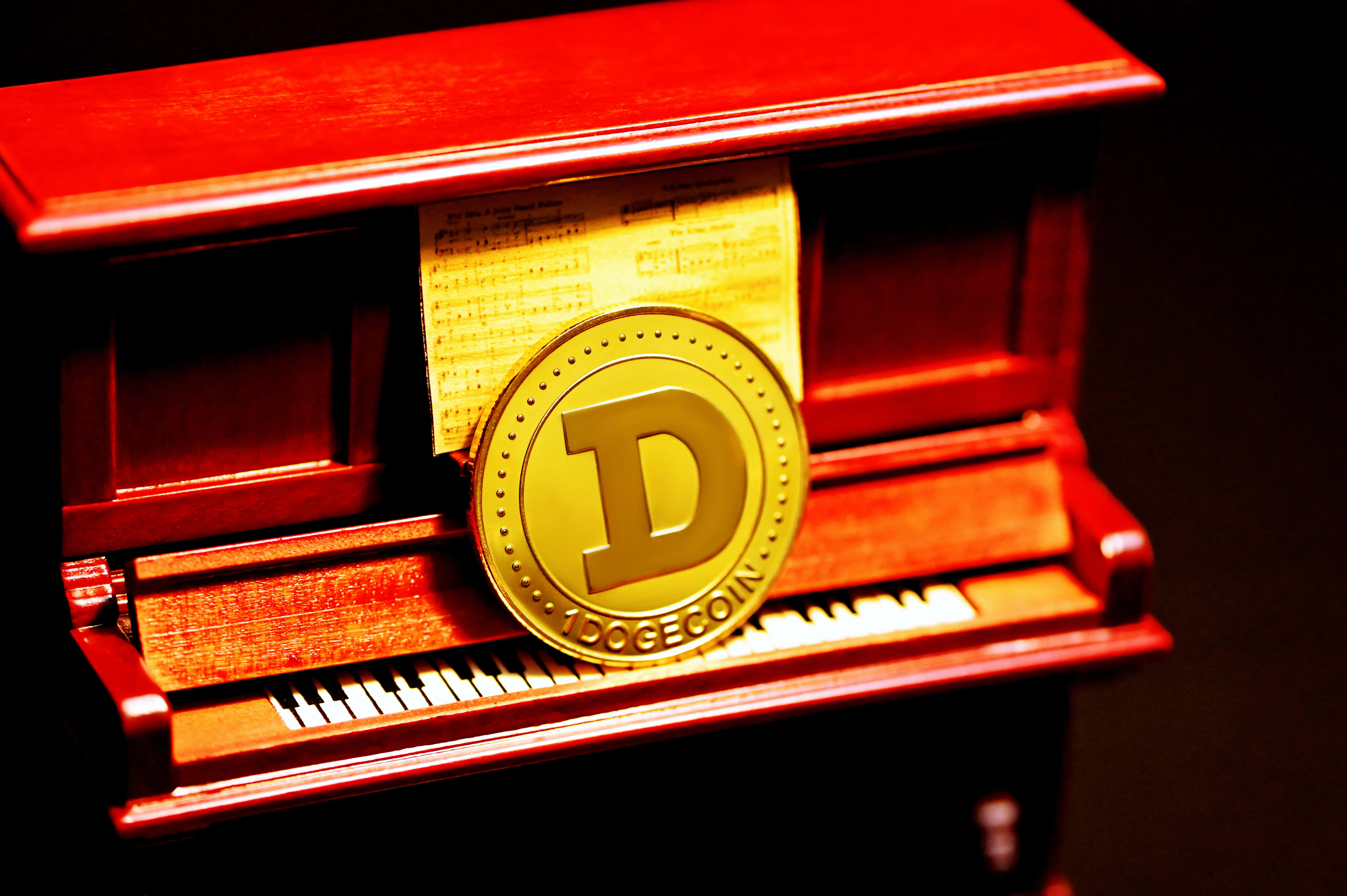 Dogecoin 桌布 壁紙 — 一枚金色Dogecoin放在紅色直立鋼琴的琴鍵上，琴譜從譜架中露出。