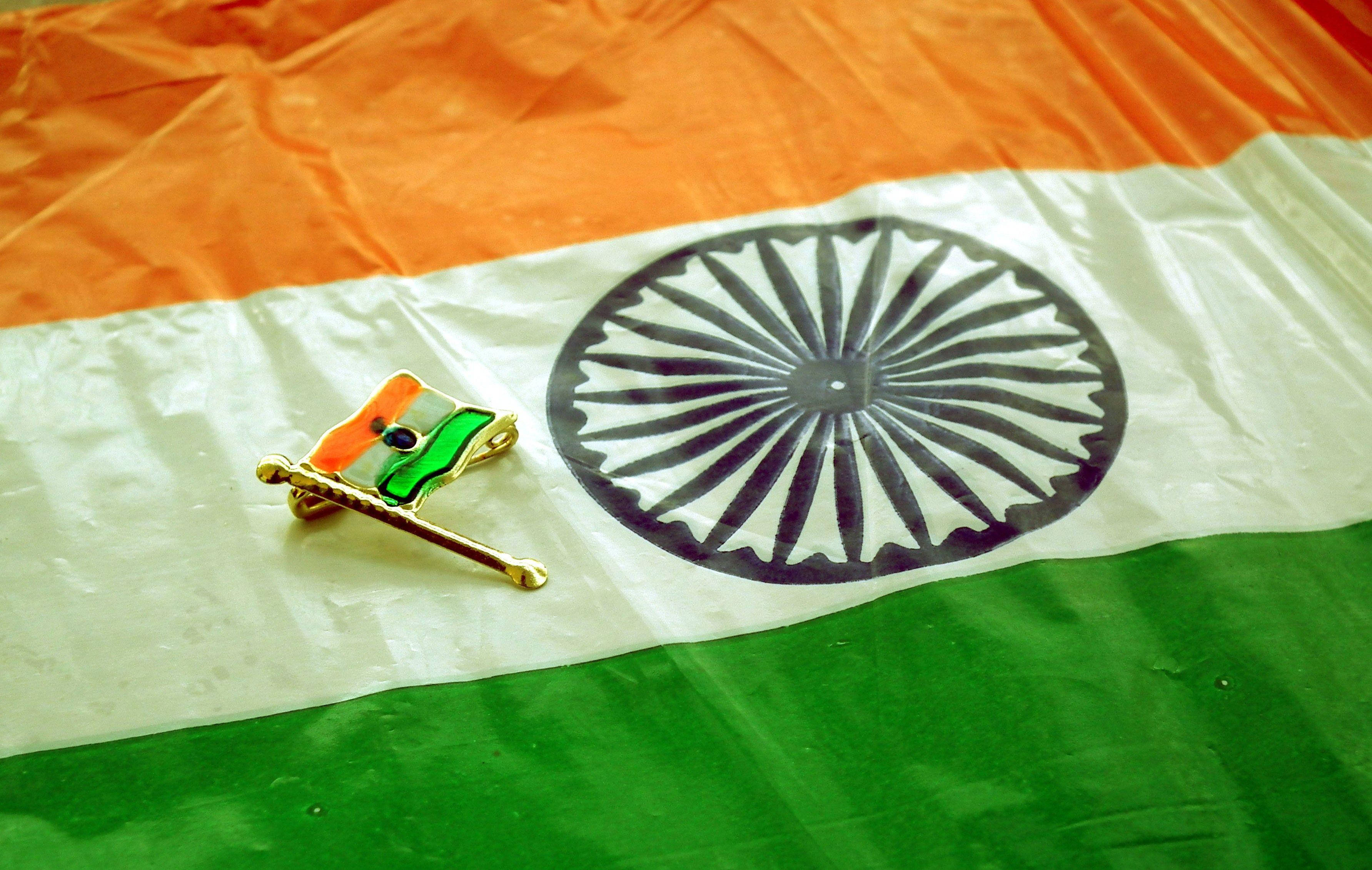 Indian 桌布 壁紙 — 一枚金色印度國旗徽章放在一面帶有藏紅花、白色和綠色條紋以及海軍藍色阿育王法輪的皺巴巴的印度國旗上。