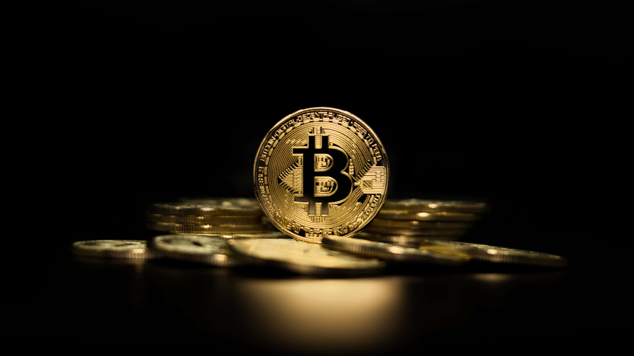 加密貨幣 桌布 壁紙 — 一枚金色比特幣硬幣在黑暗表面上散落的硬幣中直立，帶有戲劇性燈光。