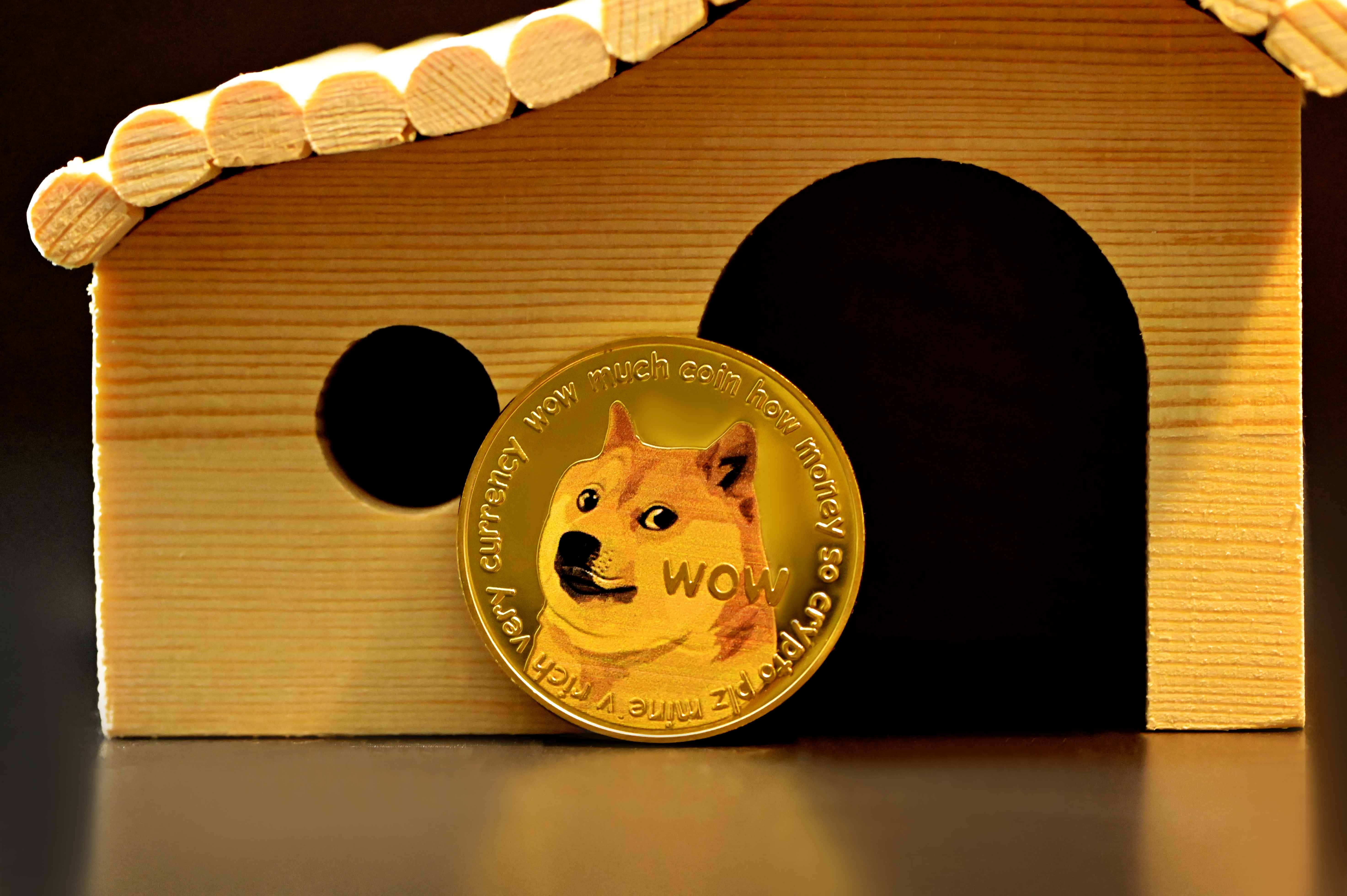 Dogecoin 桌布 壁紙 — 一枚金色狗狗幣，上面有柴犬圖案，放在一個帶拱門和圓窗的微型木製狗屋前。