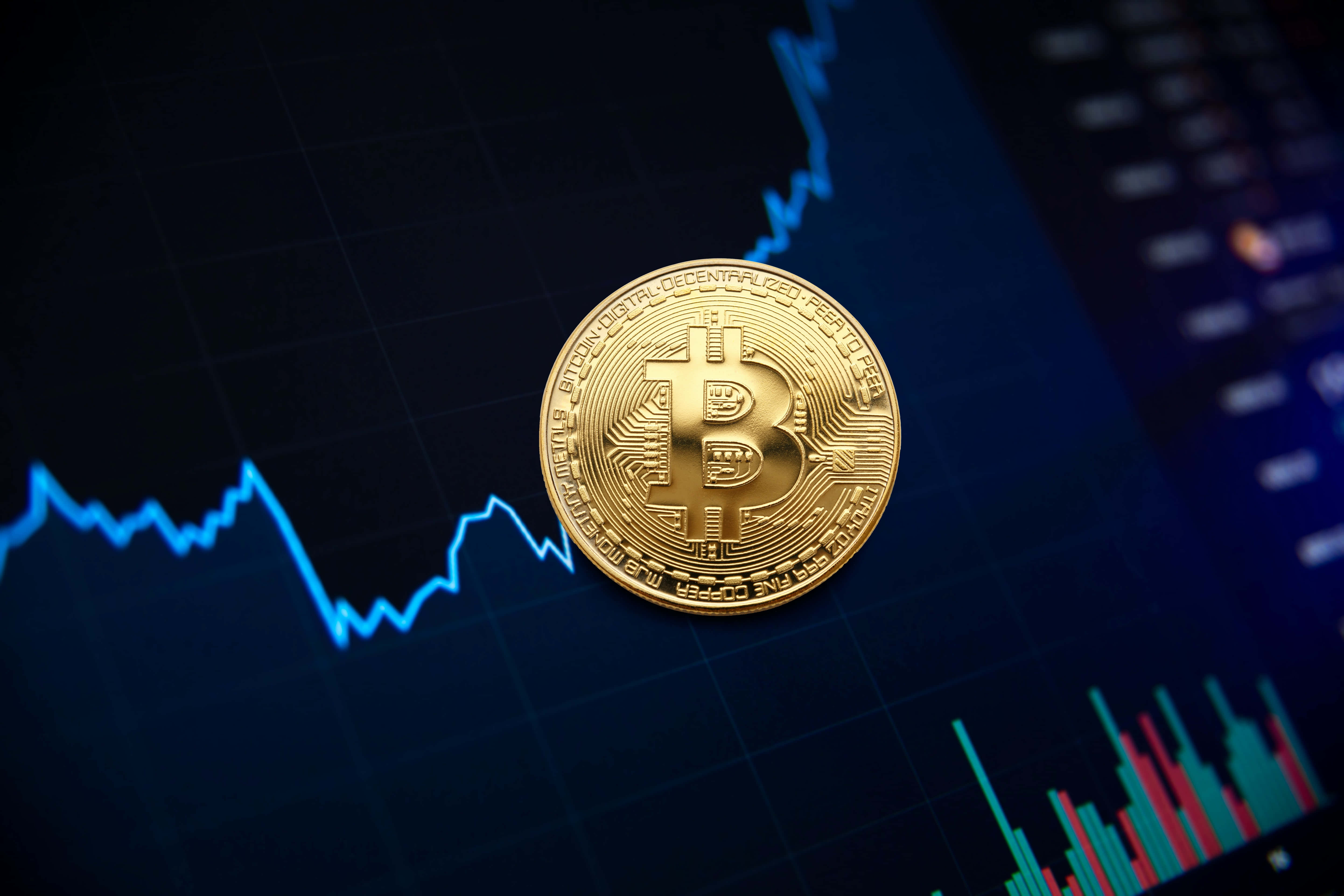 Mining 桌布 壁紙 — 一枚閃閃發光的金色比特幣硬幣放在一個顯示波動的藍色和紅色金融圖表的黑色屏幕上。
