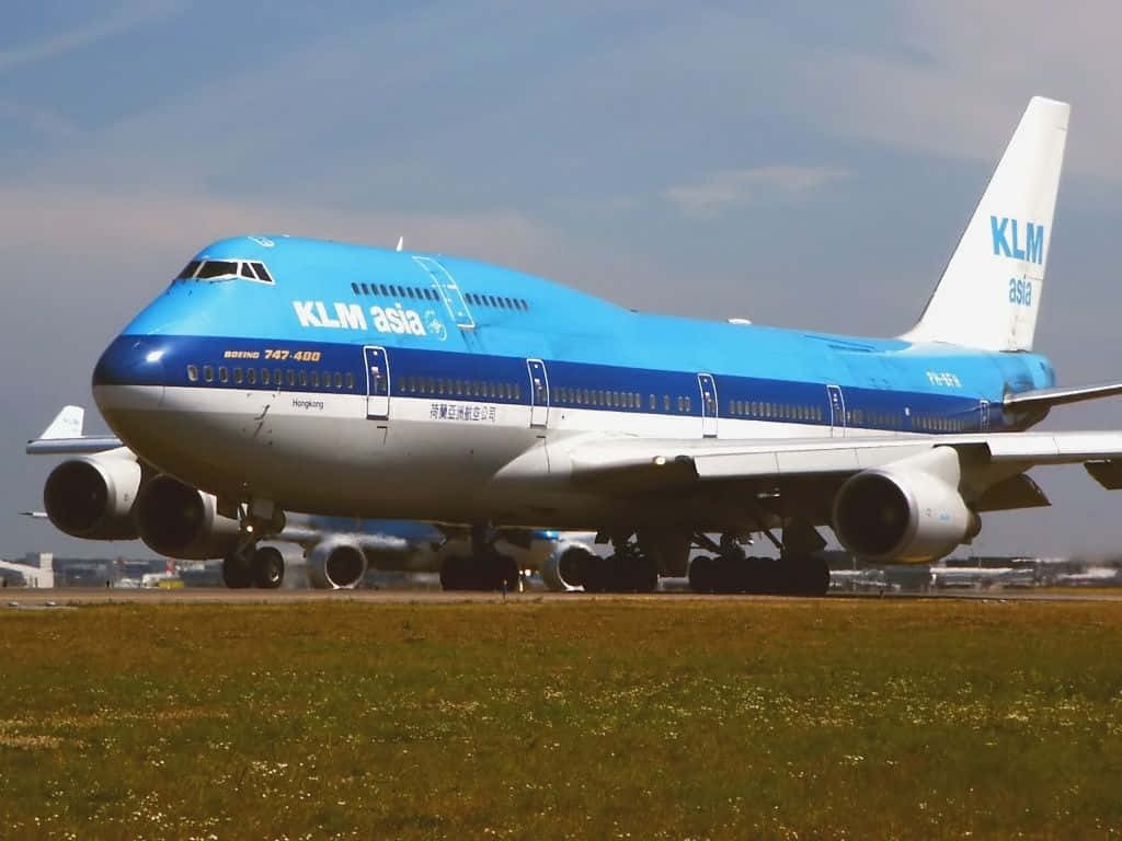 Jumbo Jets 桌布 壁紙 — 一架KLM Asia波音747-400飛機在部分多雲的天空下在草地跑道上滑行。