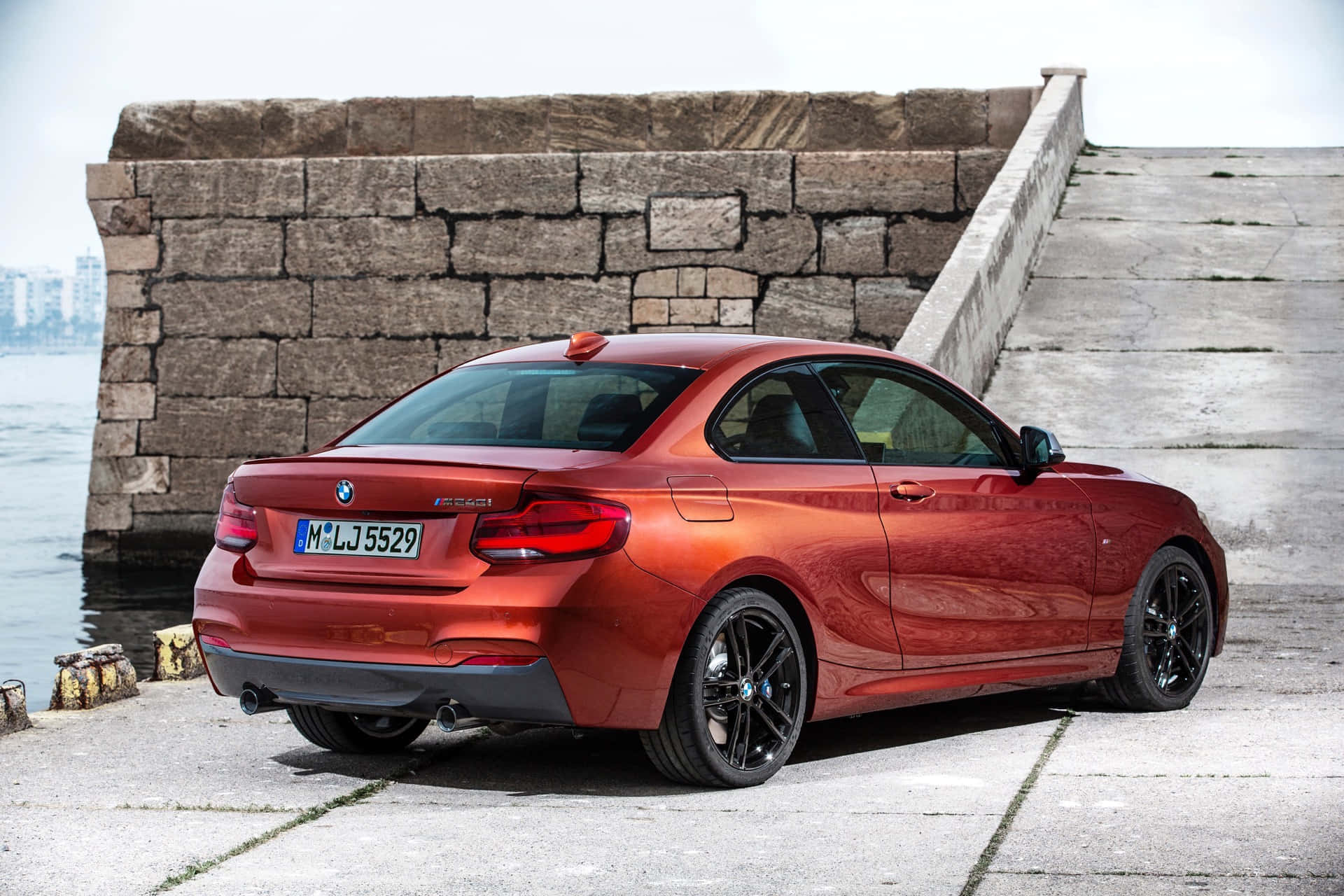 Bmw 2 Series 桌布 壁紙 — 一架亮紅色BMW 2系轎跑車停泊在風化石碼頭上，旁邊是平靜的水面，天空多雲。