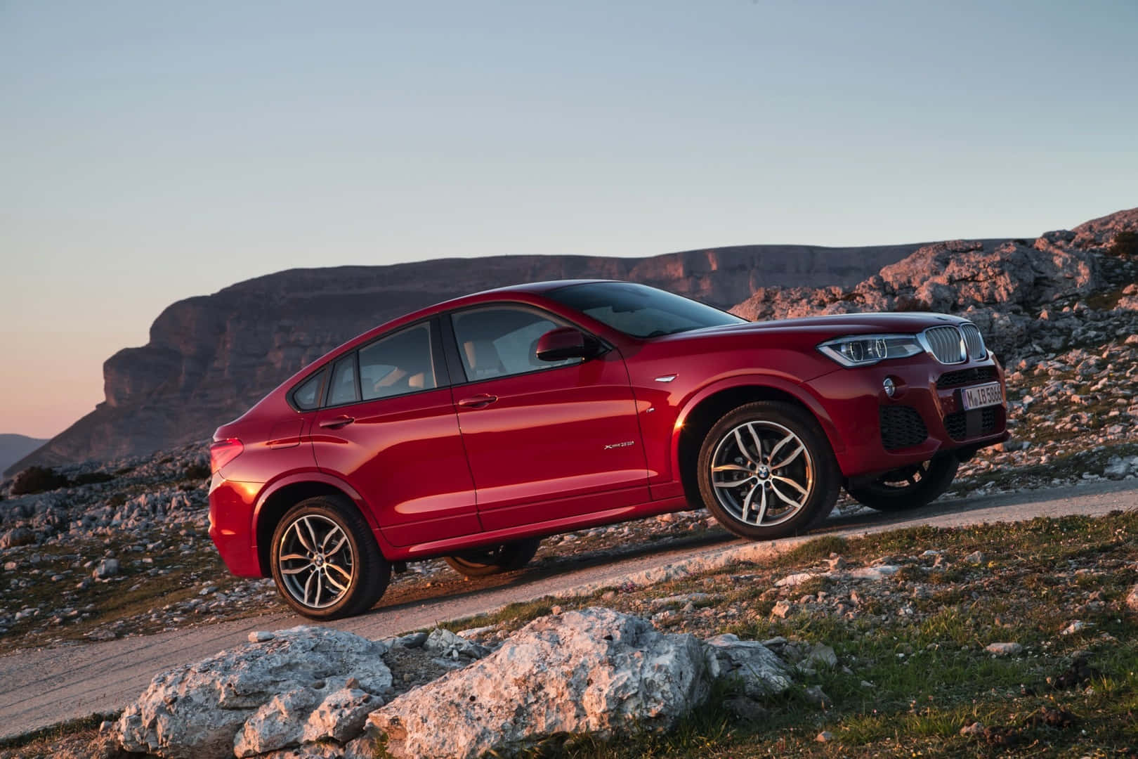 Bmw X4 桌布 壁紙 — 一架亮紅色BMW X4 SUV停泊在日落時分的岩石山路上，背景是崎嶇的懸崖。