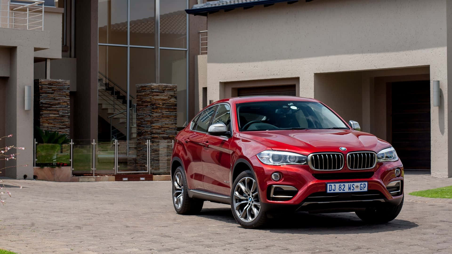 Bmw X6 桌布 壁紙 — 一架亮紅色BMW X6 SUV停泊在現代化房屋前的石頭車道上，房屋有玻璃牆和石柱。
