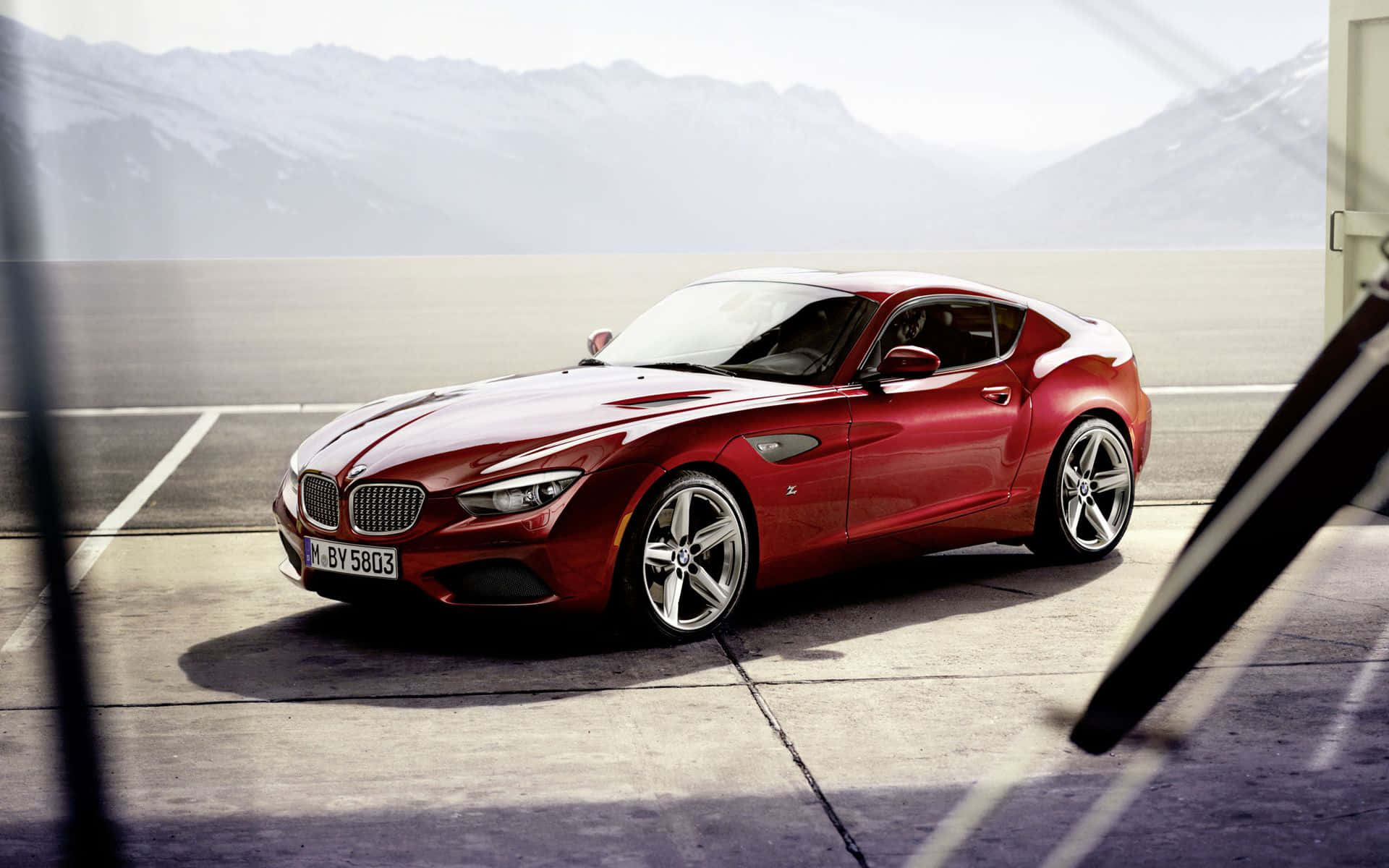 Bmw Z4 桌布 壁紙 — 一架亮紅色BMW Z4跑車停泊在混凝土場地上，背景有朦朧的雪山。
