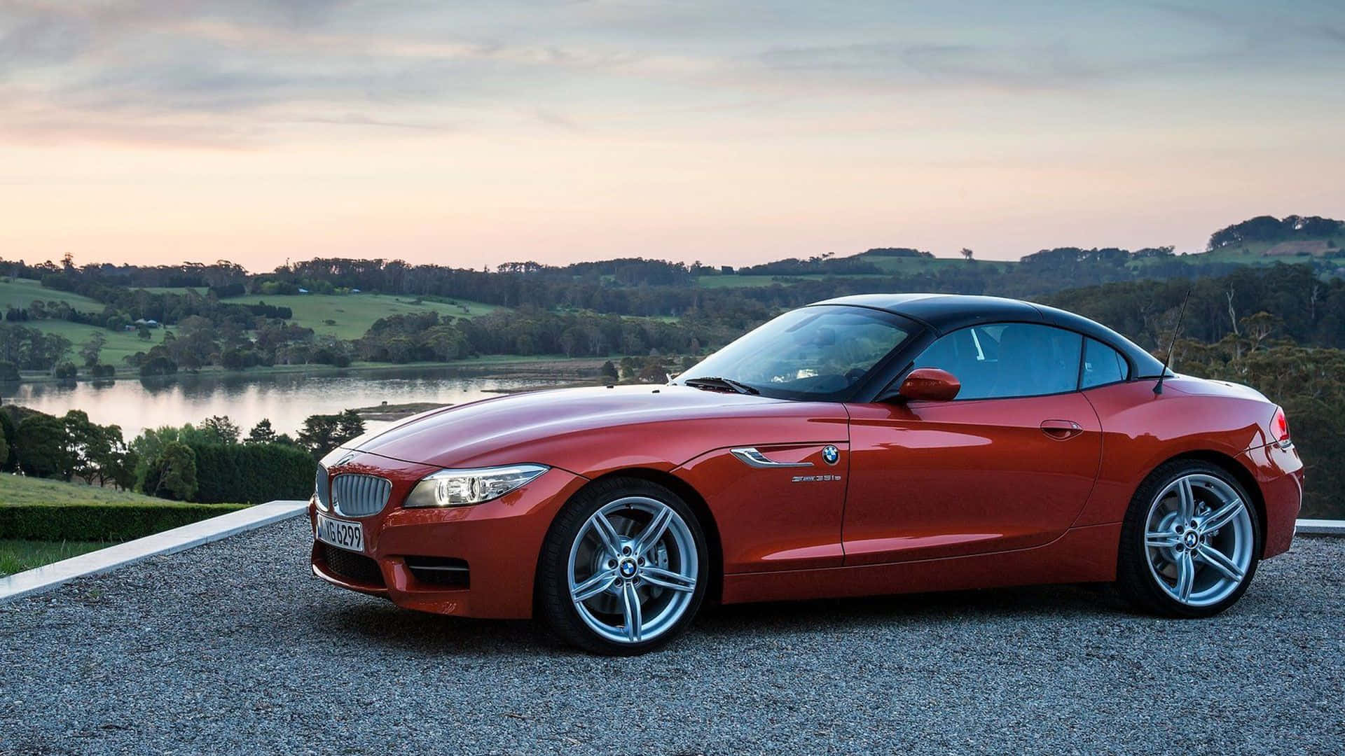 Bmw Z4 桌布 壁紙 — 一架亮紅色BMW Z4開篷跑車停泊在碎石上，俯瞰日落時分的寧靜湖泊，背景是起伏的綠色山丘。