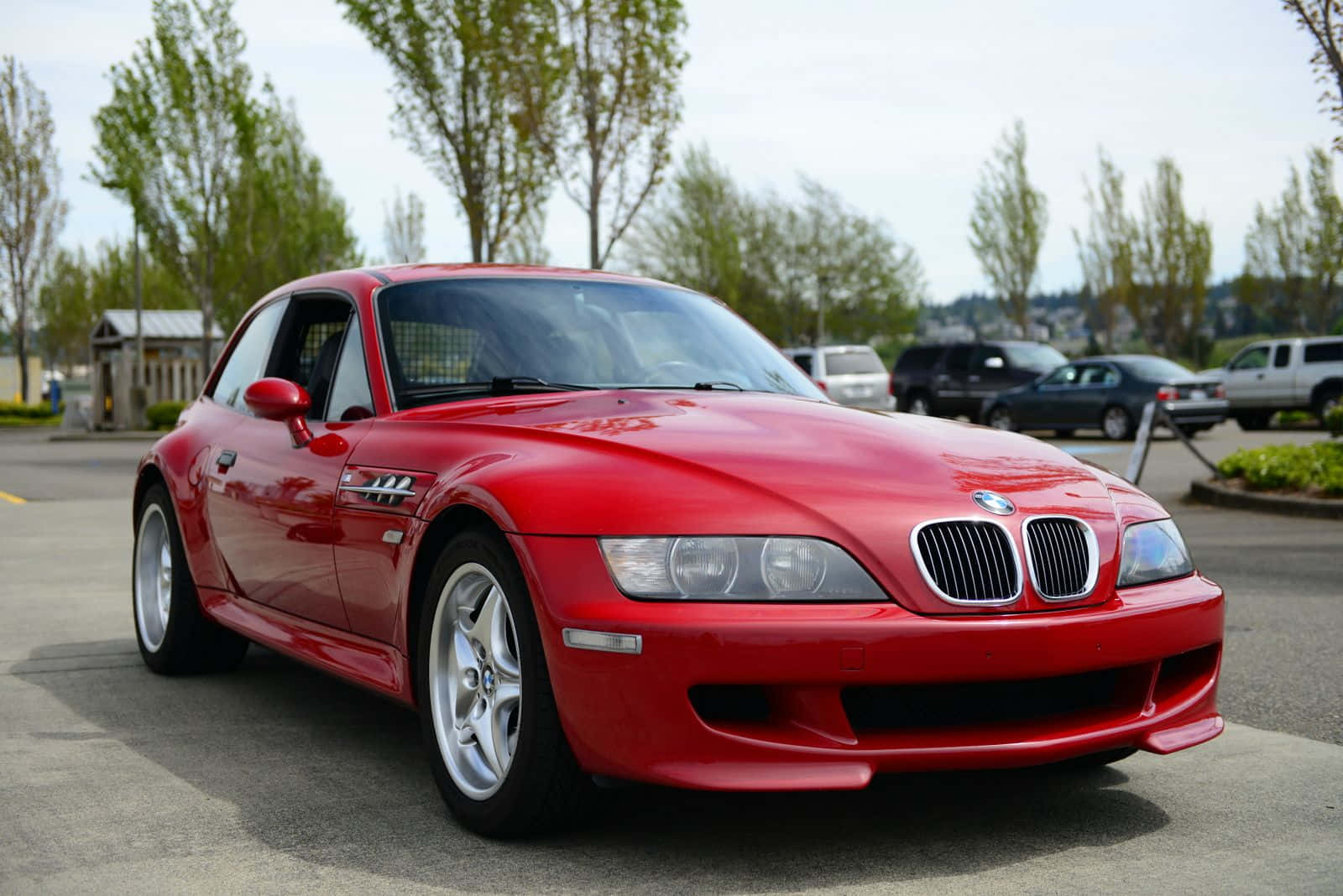Bmw Z3 桌布 壁紙 — 一架亮紅色BMW Z8跑車停泊在瀝青路上，背景有樹木及其他車輛。