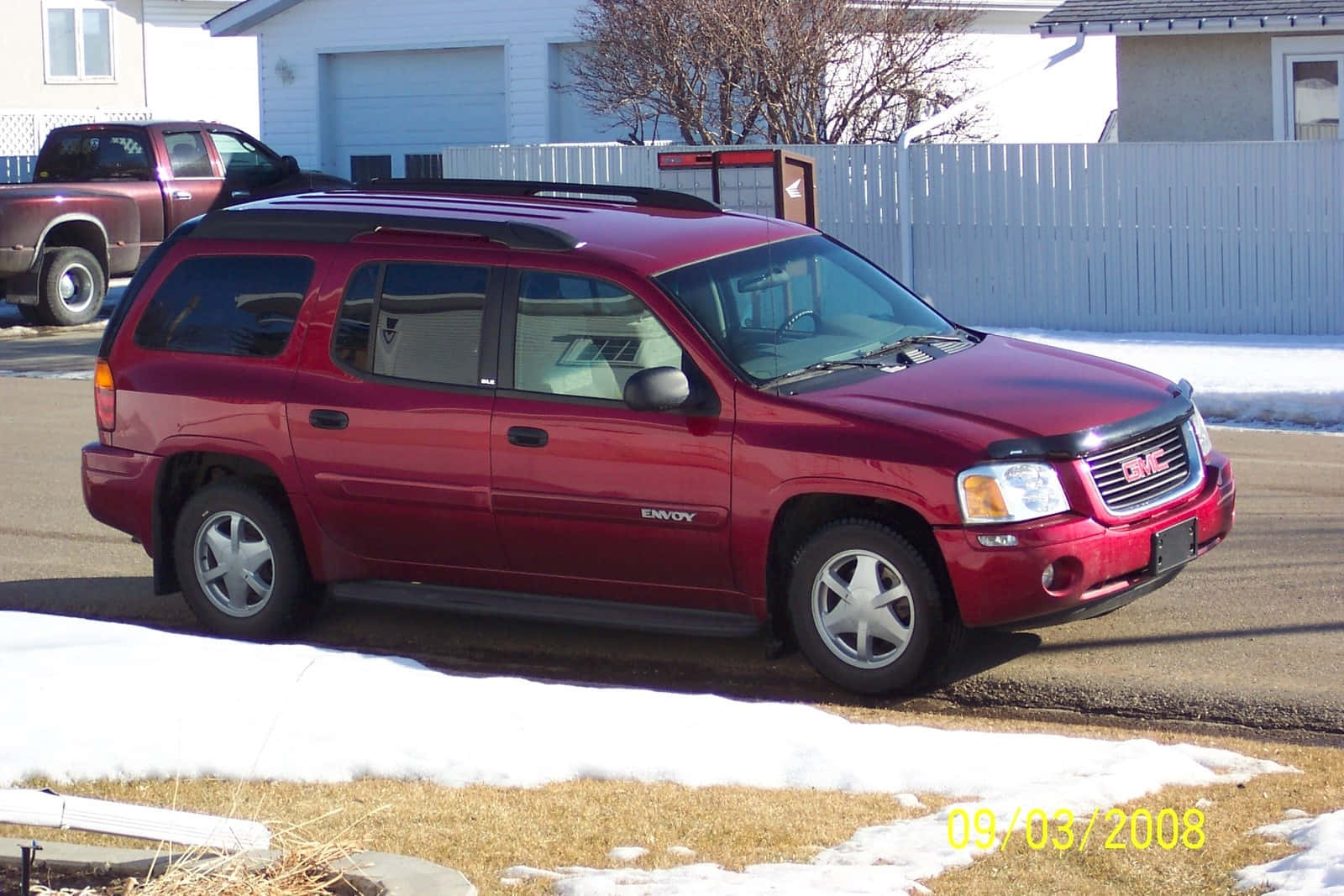 Gmc Envoy 桌布 壁紙 — 一架亮紅色GMC Envoy SUV停泊在積雪的住宅街道上，背景有白色圍欄和光禿禿的樹木。