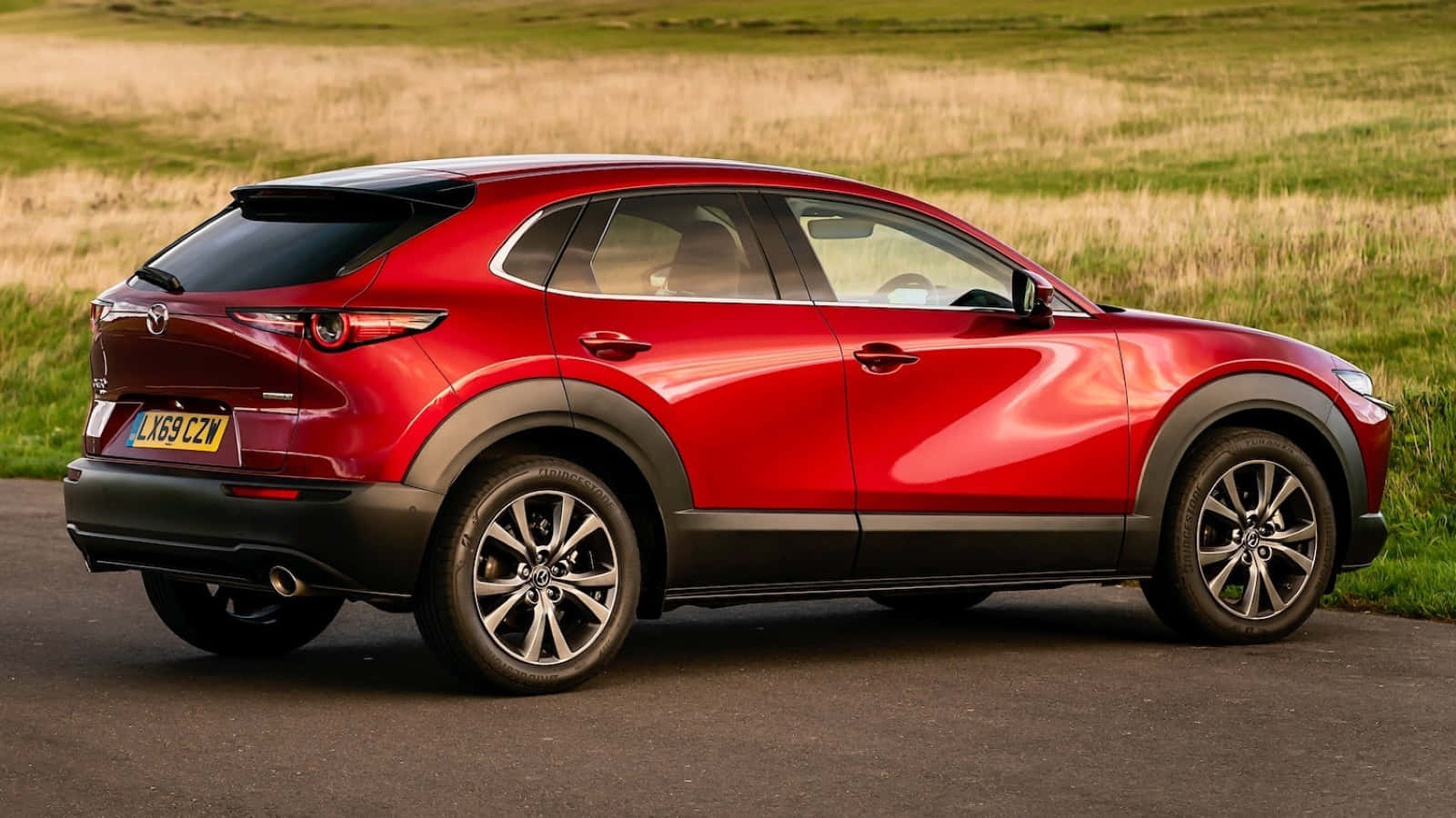 Mazda Cx-30 桌布 壁紙 — 一架亮紅色Mazda CX-3 SUV停泊在路邊，旁邊是金色草地，在柔和日光下。