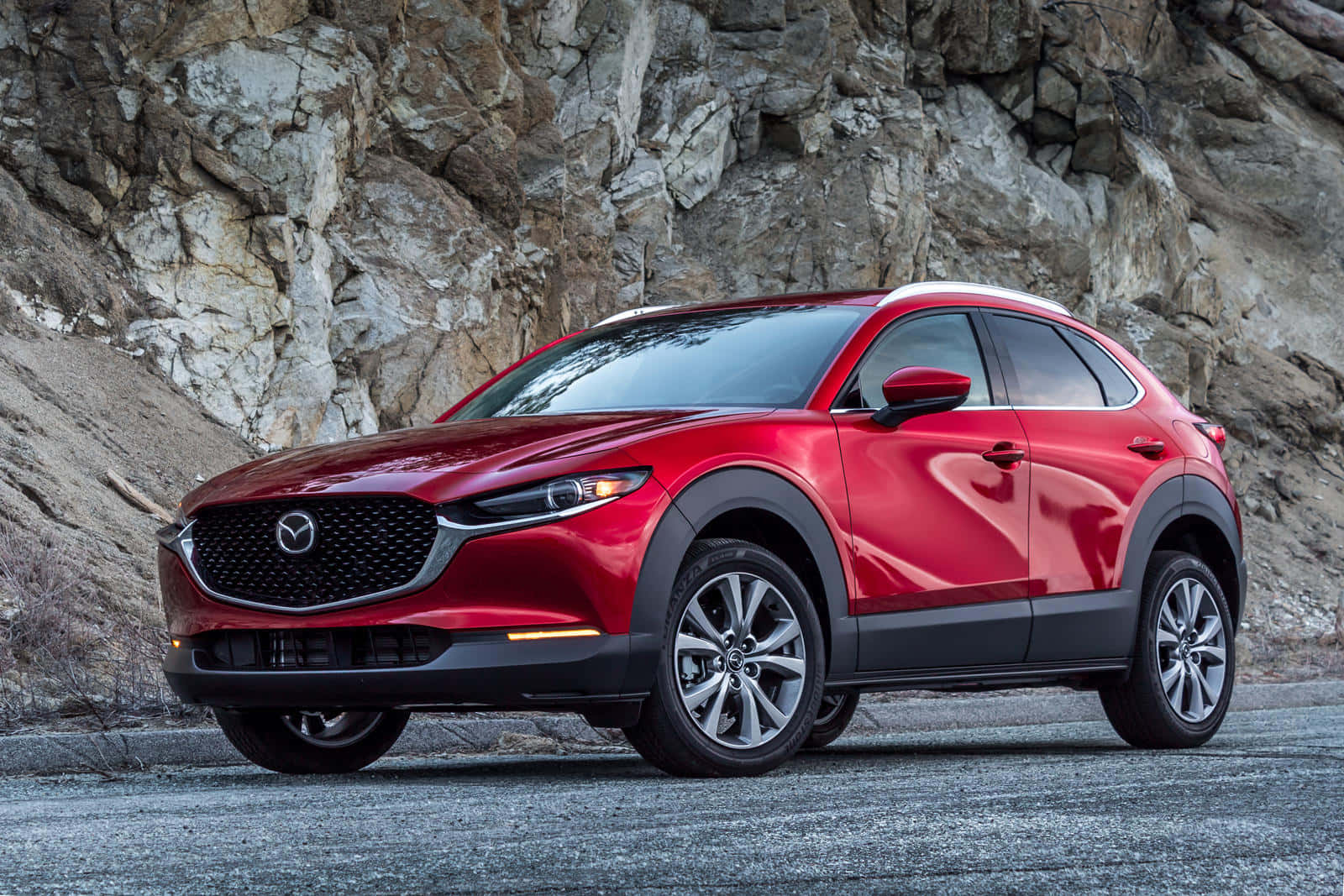 Mazda Cx-30 桌布 壁紙 — 一架亮紅色Mazda CX-30 SUV停泊在崎嶇岩石懸崖前的碎石路上。