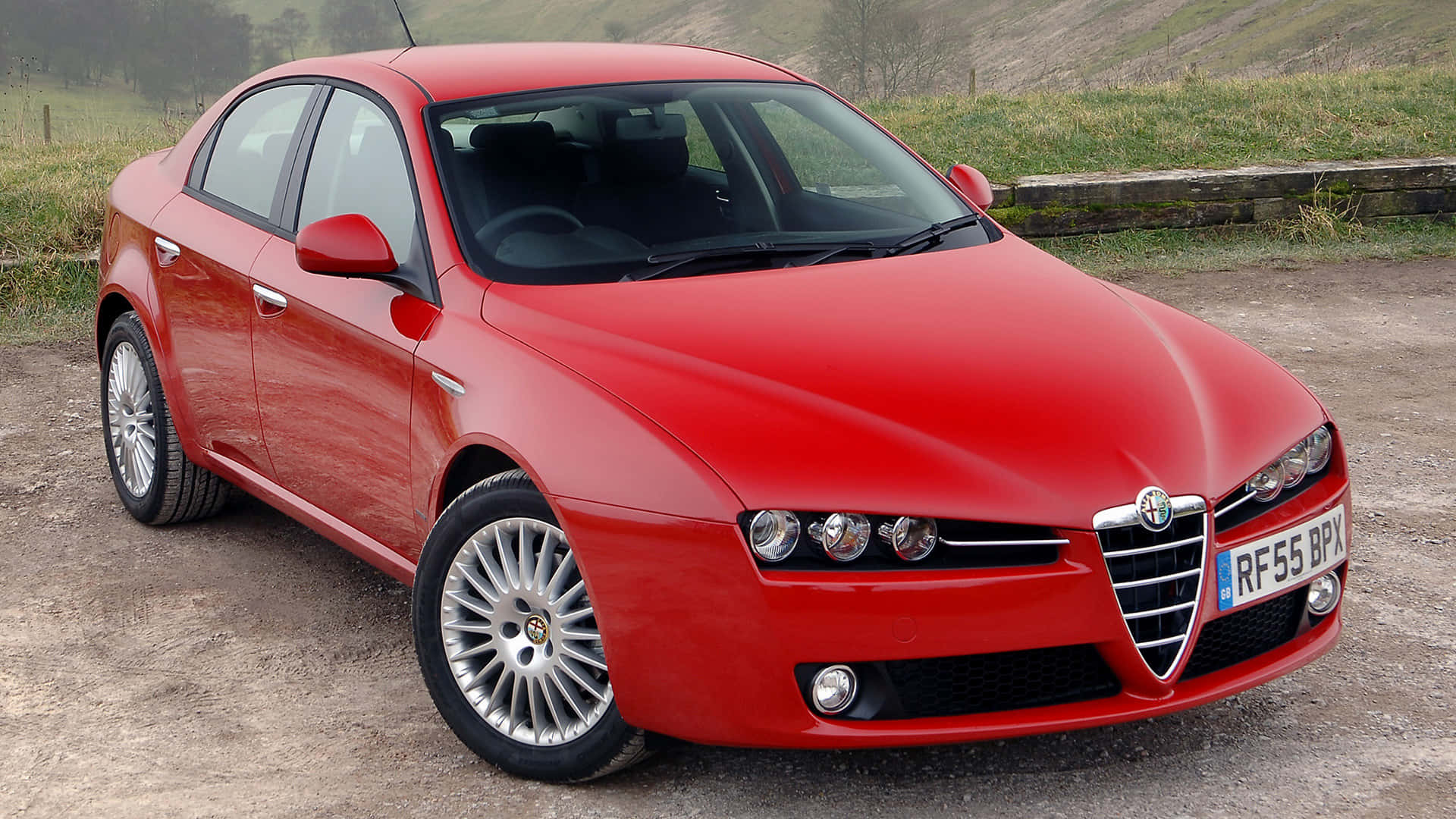 Alfa Romeo 159 桌布 壁紙 — 一架亮紅色嘅Alfa Romeo房車停泊喺碎石上，背景有綠色山丘同石牆。