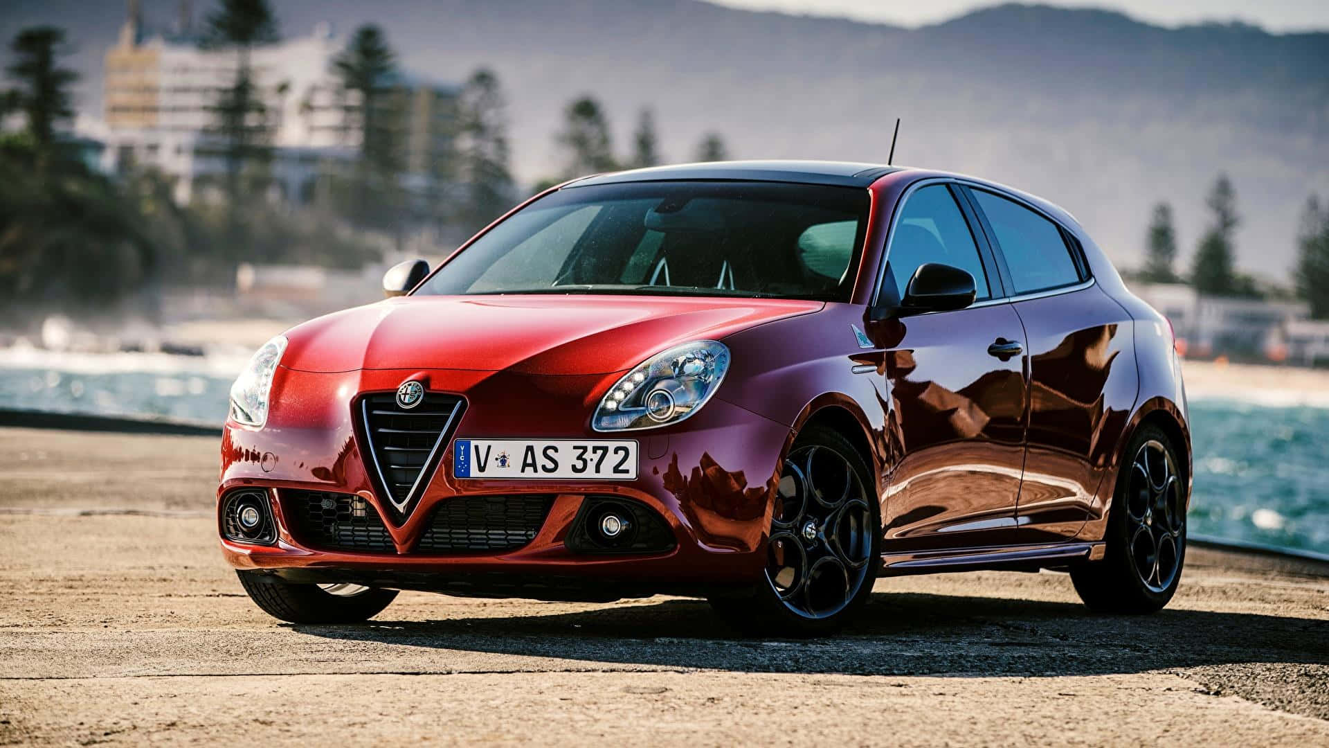 Alfa Romeo Giulia 桌布 壁紙 — 一架亮紅色嘅Alfa Romeo Giulietta停泊喺沿海公路，背景係海洋同山丘。