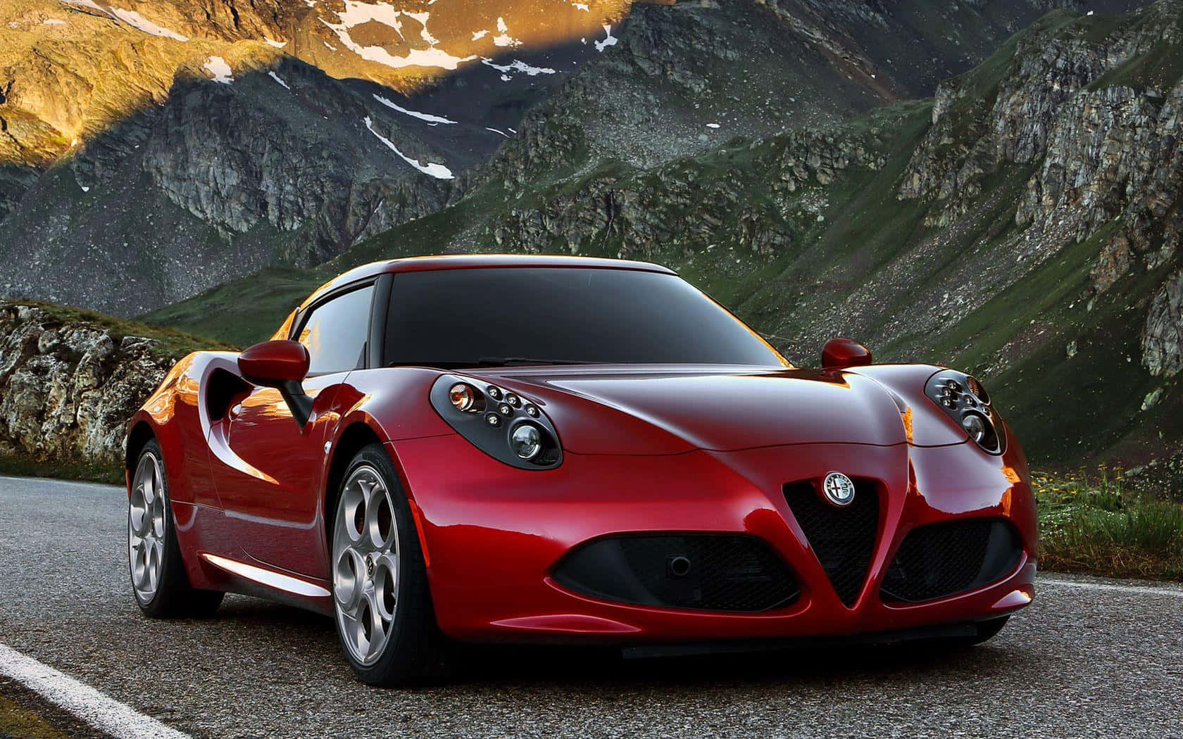 Alfa Romeo 4c 桌布 壁紙 — 一架亮紅色嘅Alfa Romeo跑車停泊喺一條山路，周圍係被金色夕陽照住嘅積雪山峰。