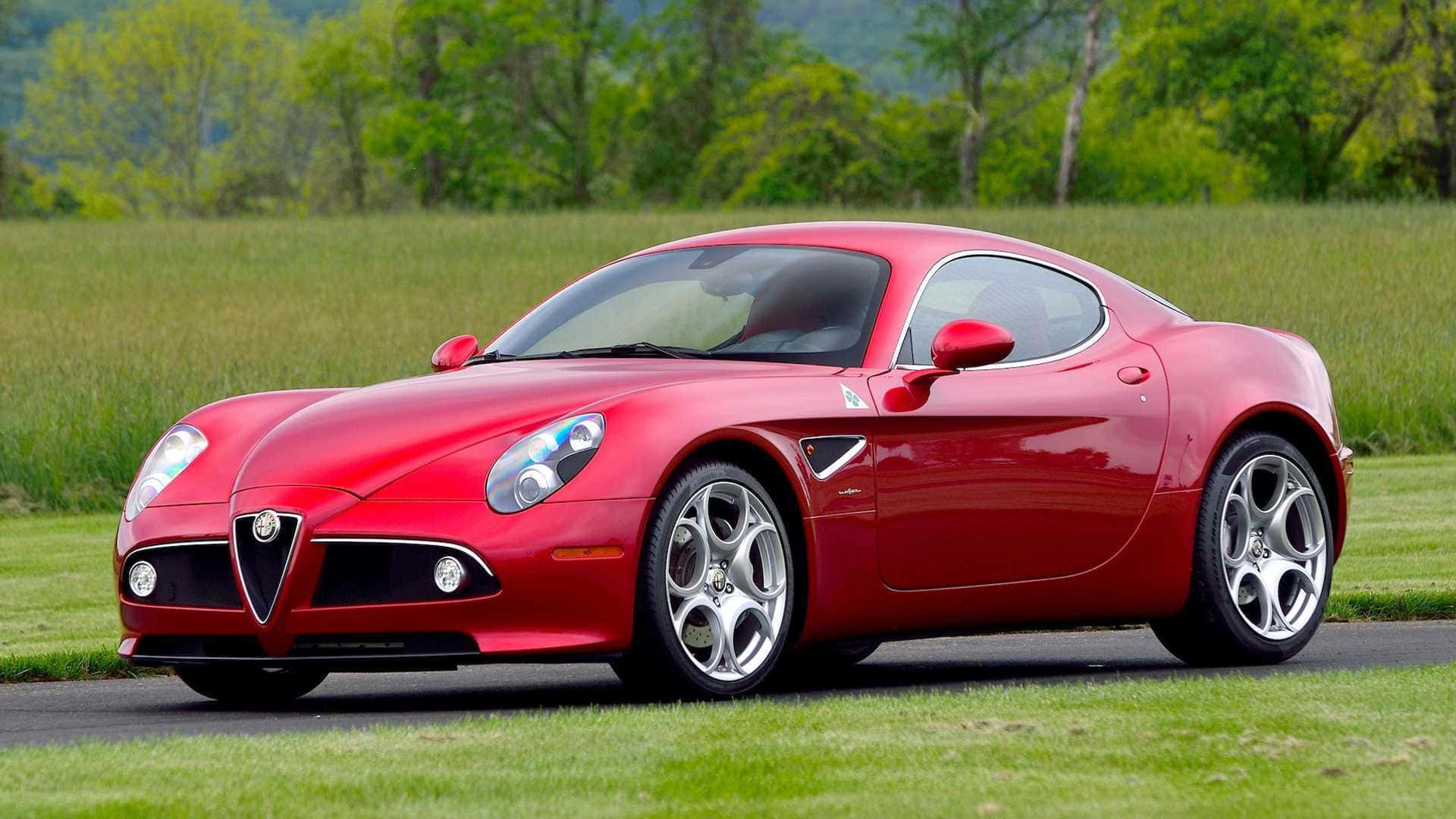 Alfa Romeo 8c Competizione 桌布 壁紙 — 一架亮紅色嘅Alfa Romeo跑車停泊喺鋪砌嘅道路上，旁邊係一片草地，背景有綠色樹木。