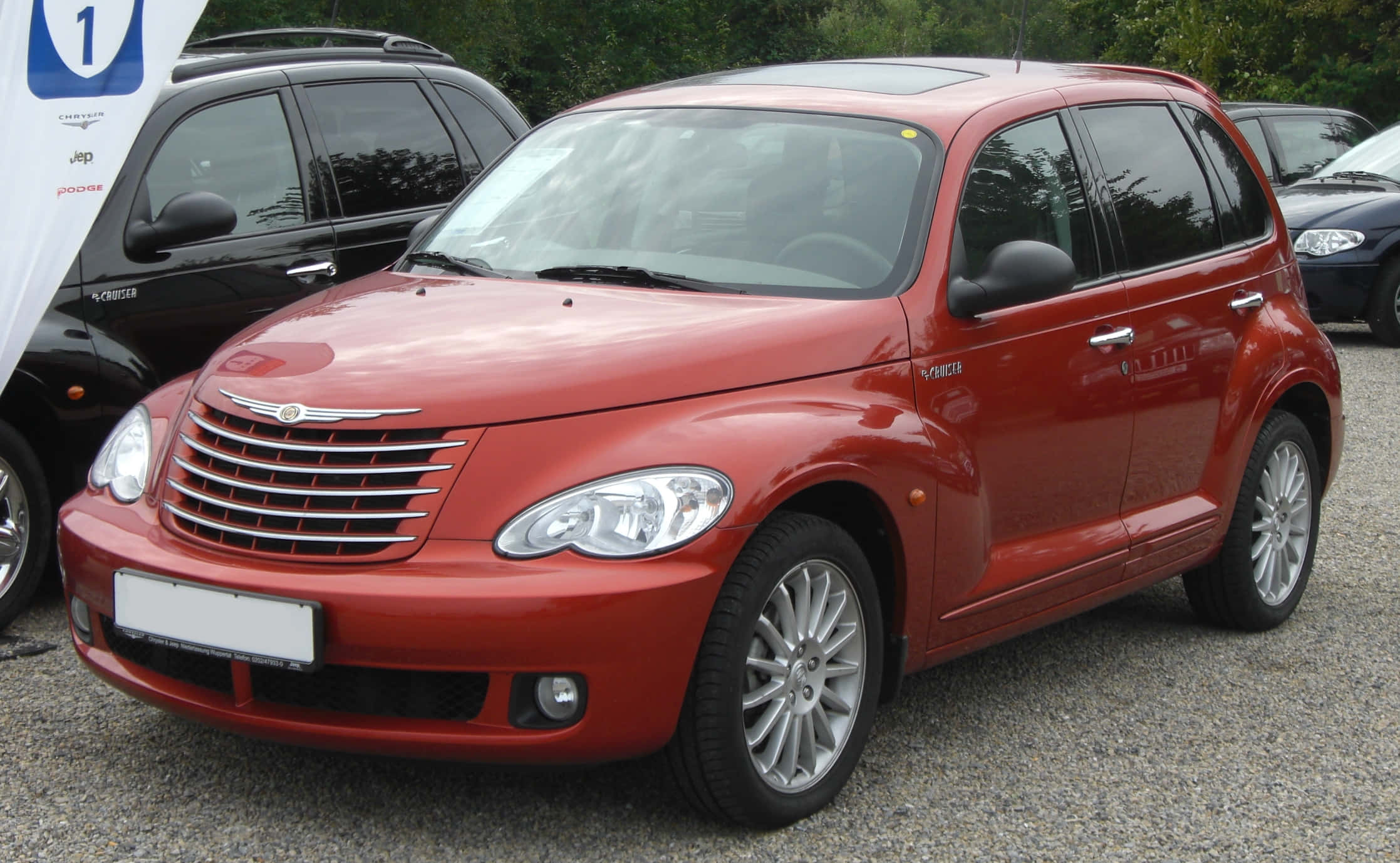 Chrysler Pt Cruiser 桌布 壁紙 — 一架亮紅色嘅Chrysler PT Cruiser泊喺碎石上，背景有樹木。