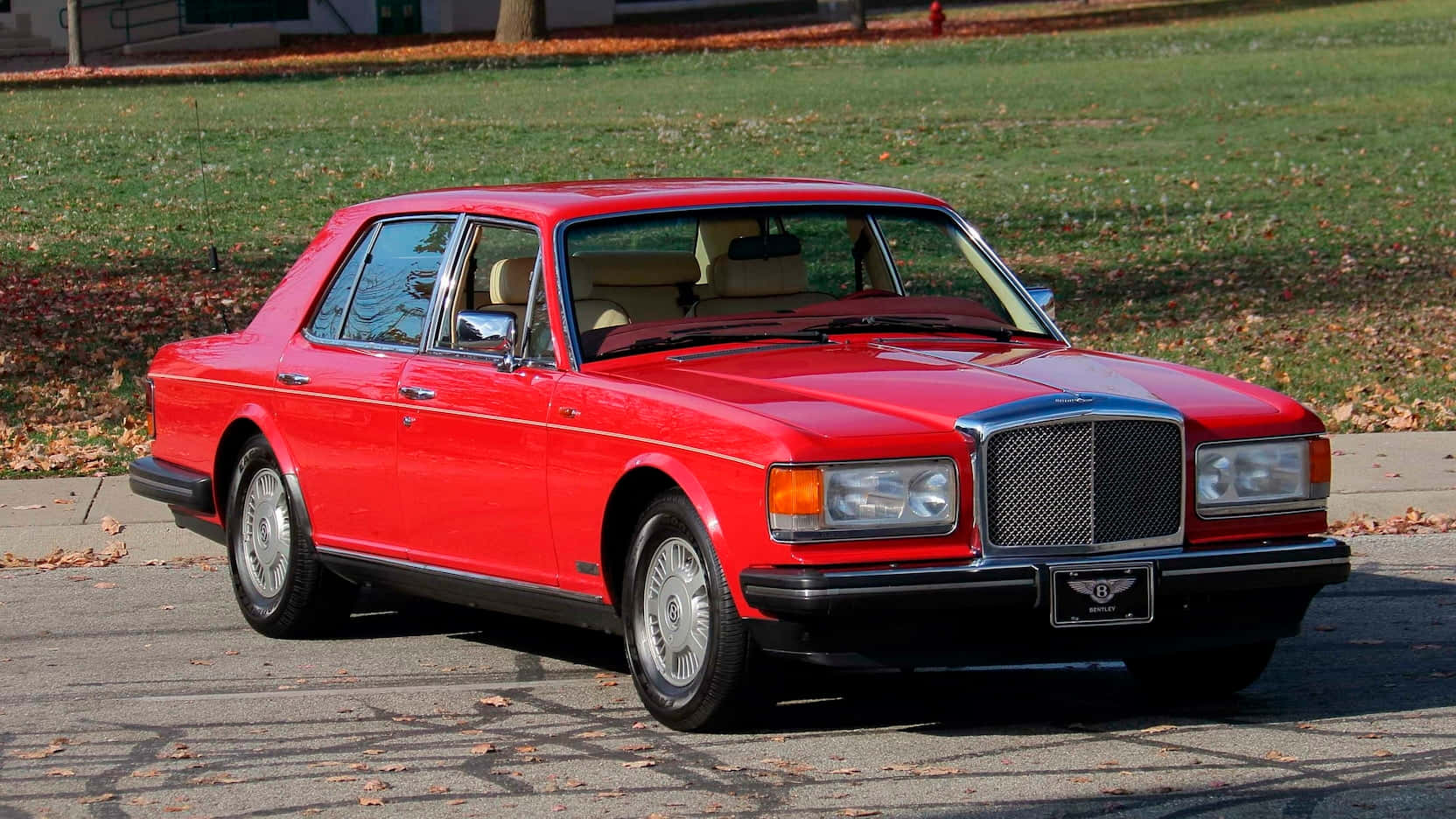 Bentley Eight 桌布 壁紙 — 一架亮紅色嘅賓利房車停泊喺鋪滿落葉嘅車道上，背景有秋天嘅草同樹。