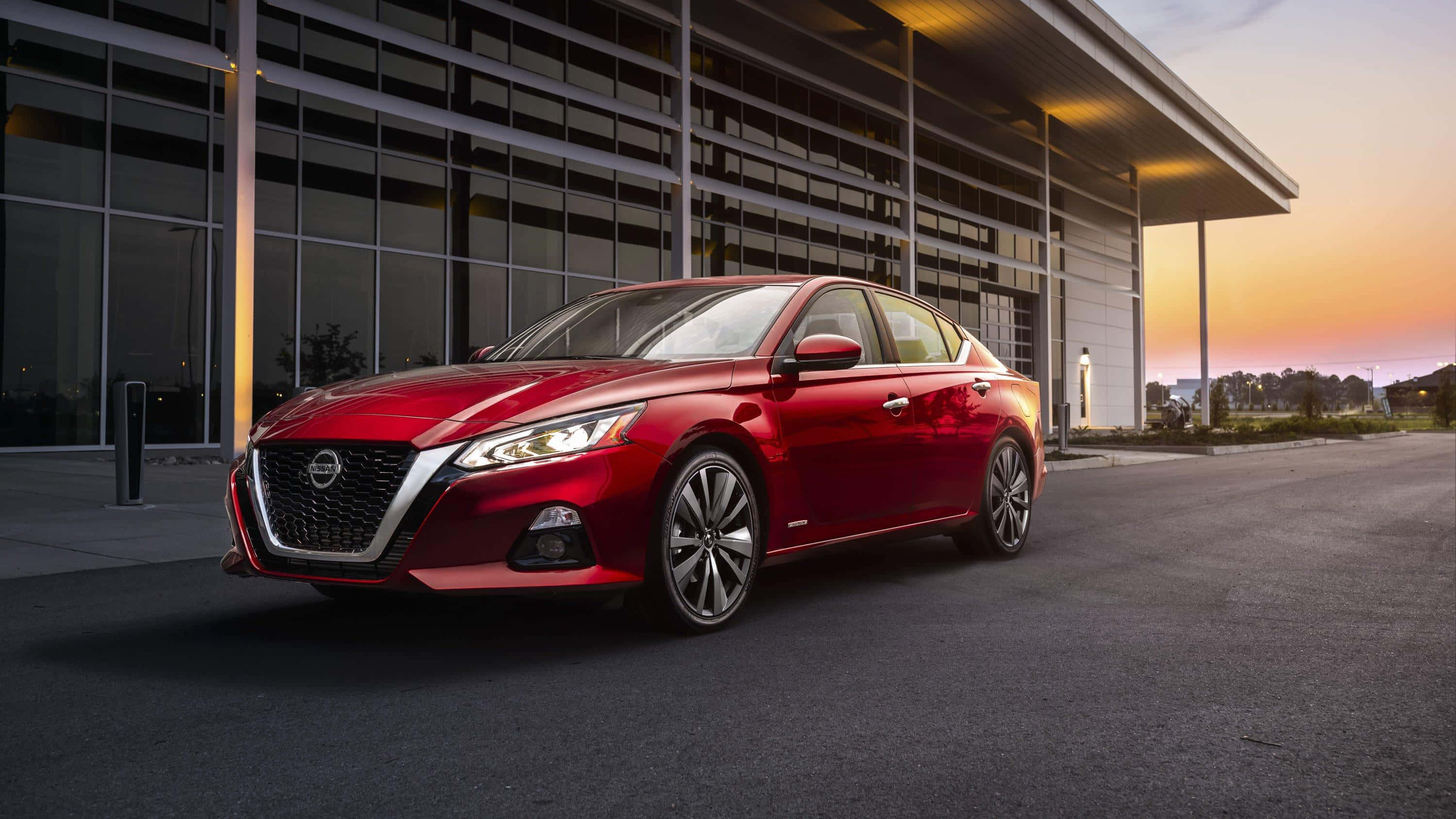 Nissan Altima 桌布 壁紙 — 一架亮紅色日產Altima房車停泊在現代玻璃建築前，正值溫暖的日落時分。