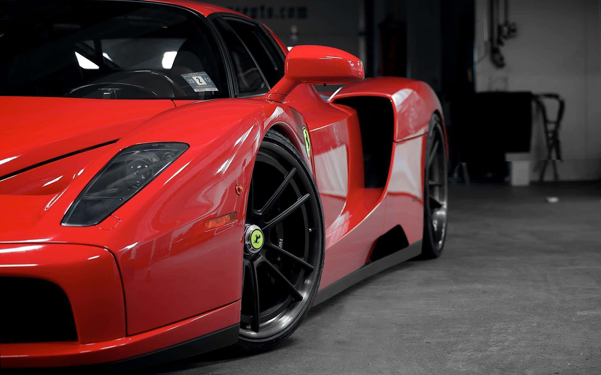 Ferrari Enzo 桌布 壁紙 — 一架亮紅色法拉利Enzo跑車停泊在燈光昏暗的車庫中，配備黑色車輪和綠色中心蓋。