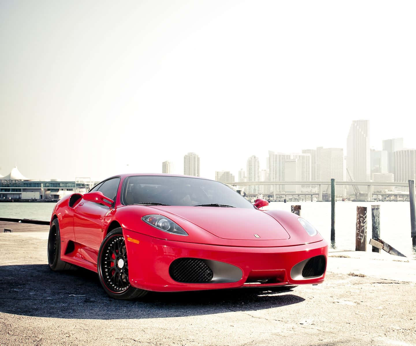 Ferrari 360 Modena 桌布 壁紙 — 一架亮紅色法拉利F430跑車停泊在海濱碼頭，背景是模糊的城市天際線。