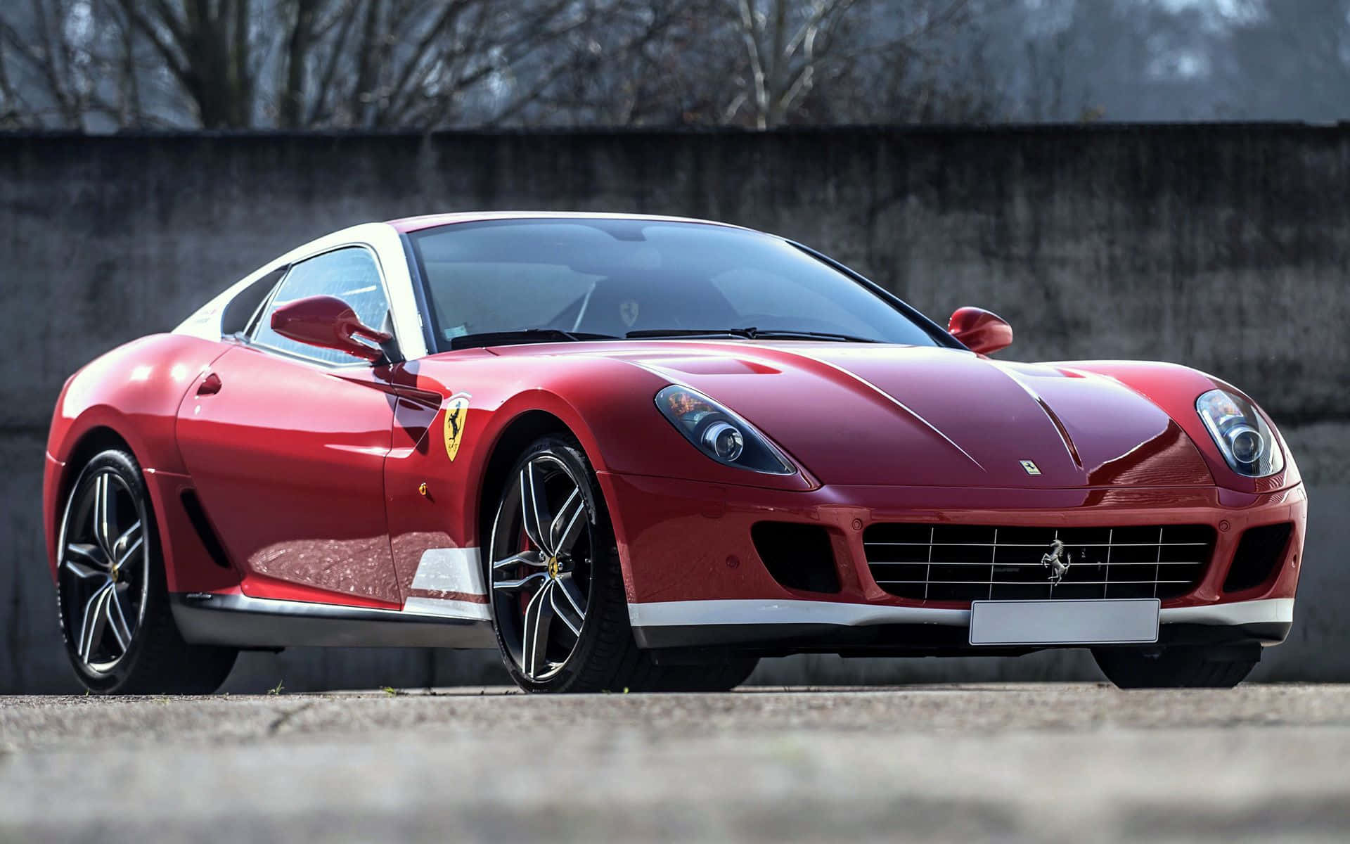 Ferrari 599 Gtb Fiorano 桌布 壁紙 — 一架亮紅色法拉利跑車停在混凝土上，背景有光禿禿的樹木和灰色牆壁。