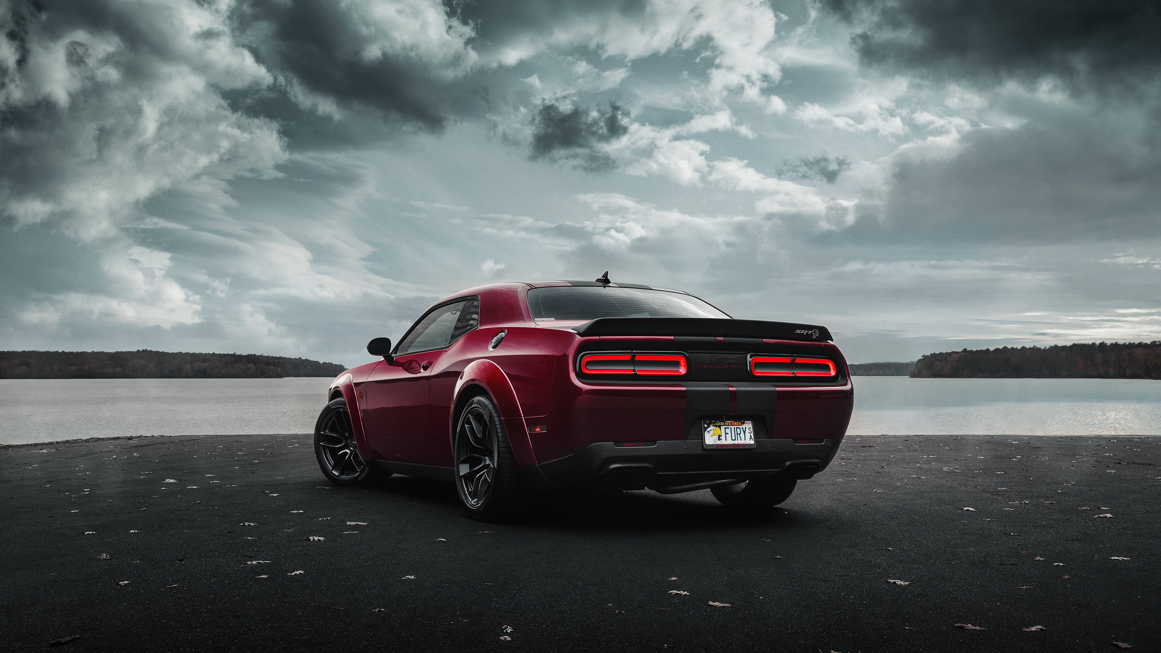 Cool Car 桌布 壁紙 — 一架亮紅色的道奇挑戰者停泊在平靜的湖邊，深色瀝青岸邊，天空烏雲密佈，氣氛戲劇化。