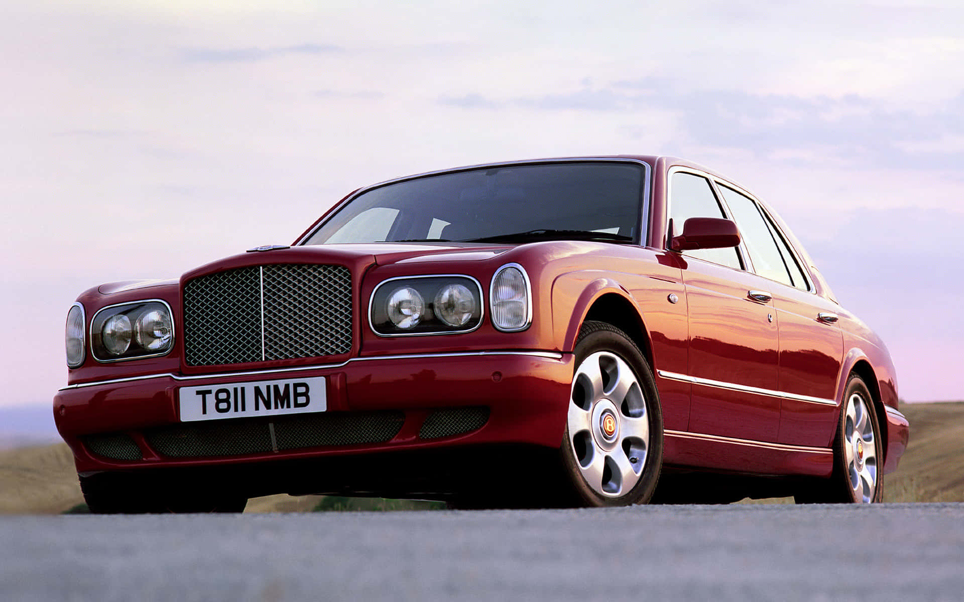 Bentley Arnage 桌布 壁紙 — 一架亮紅色賓利 Continental 豪華轎車停泊在鋪砌道路上，背景是柔和嘅暮色天空。