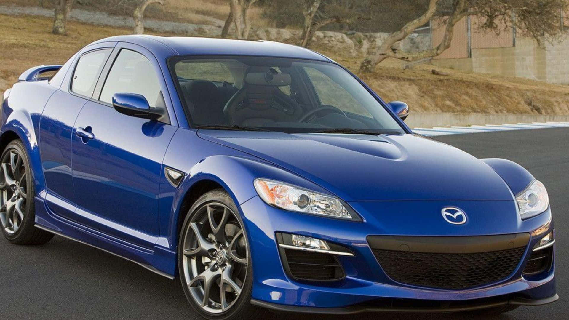 Mazda Rx-8 桌布 壁紙 — 一架亮藍色Mazda RX-8跑車停泊在瀝青賽道上，背景有乾草和樹木。