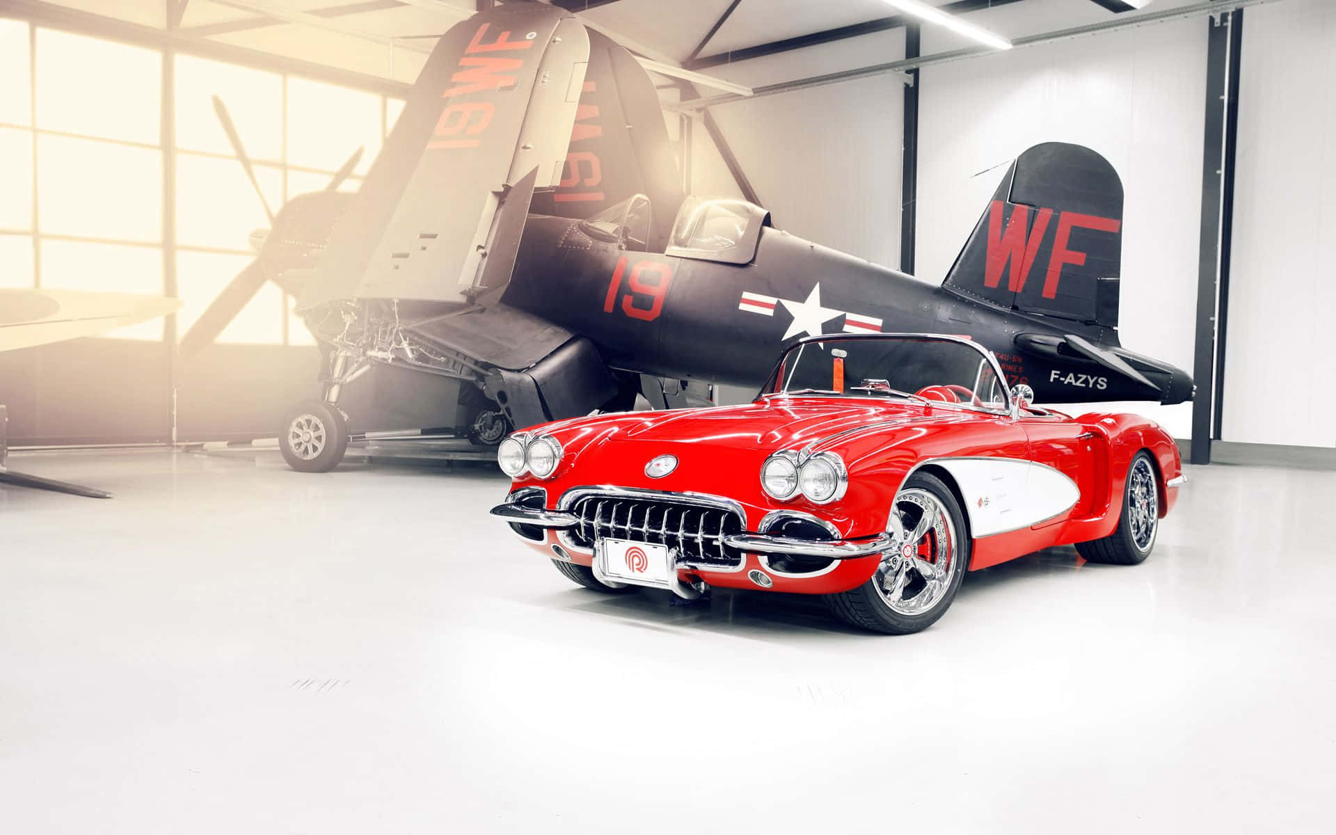 classic 桌布 壁紙 — 一架亮面紅色經典Corvette開篷跑車停泊在明亮的機庫內，前面是一架復古軍用戰鬥機。